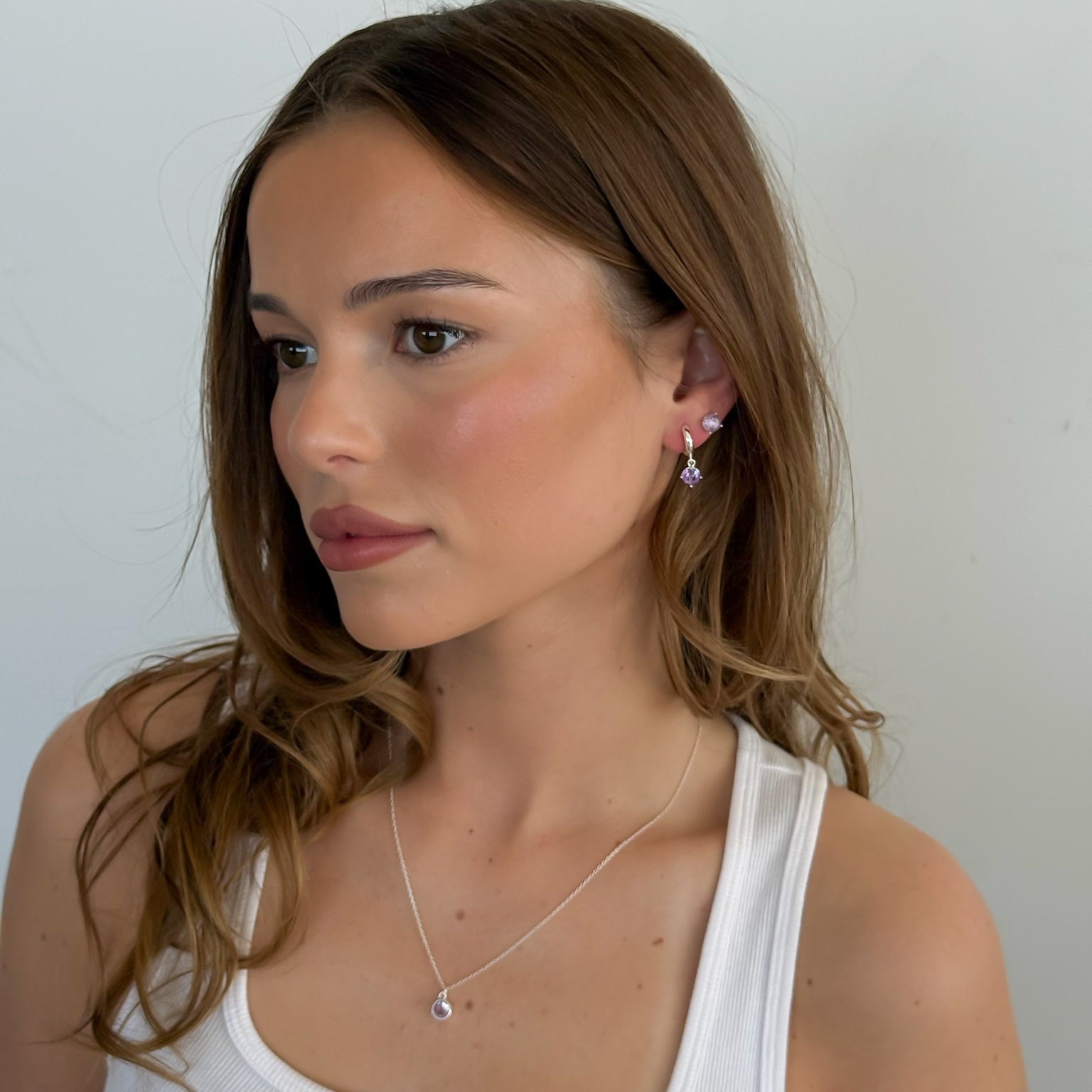 Woman wearing a white tank top and gold necklace against a plain background