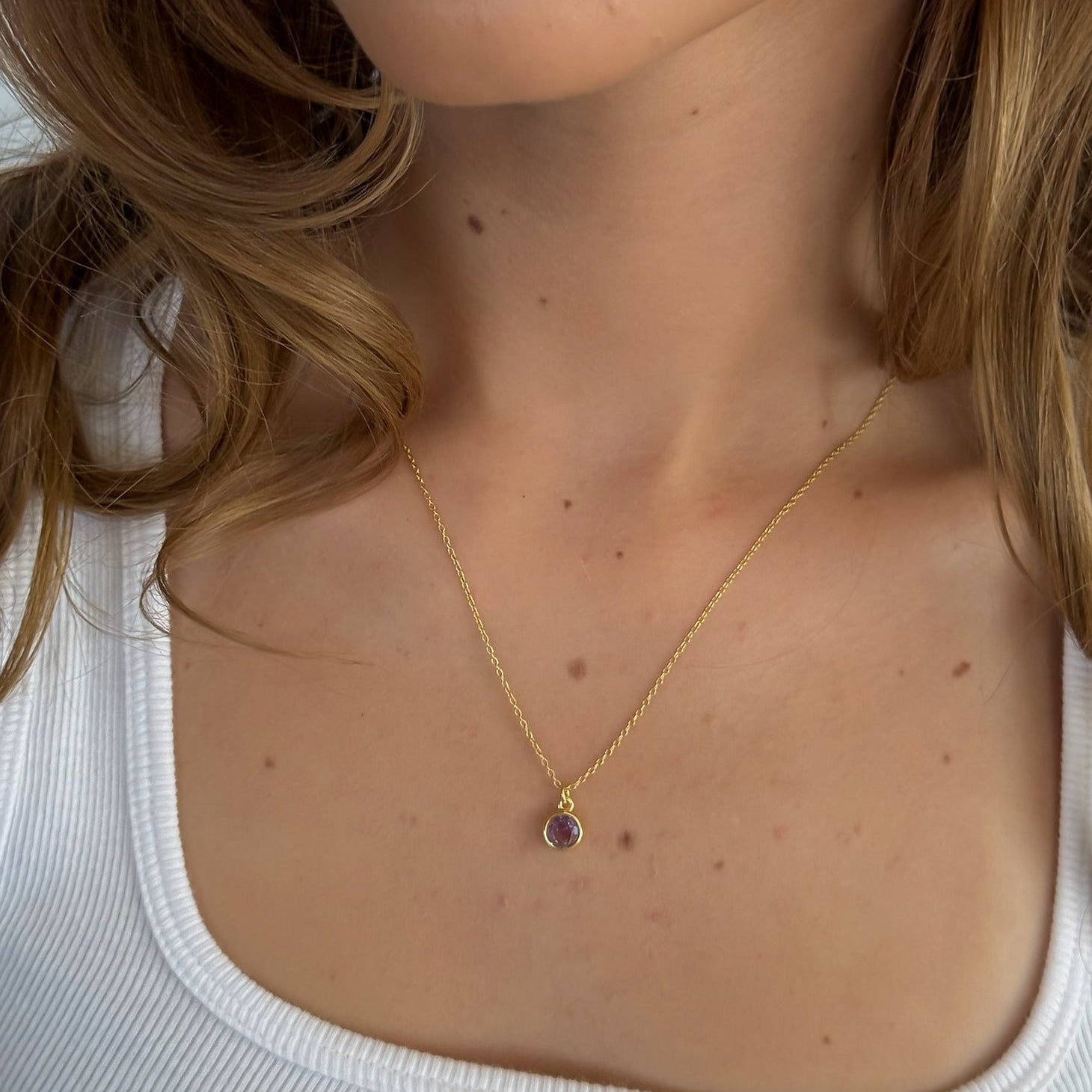 Close-up of a person wearing a gold necklace with a small pendant.