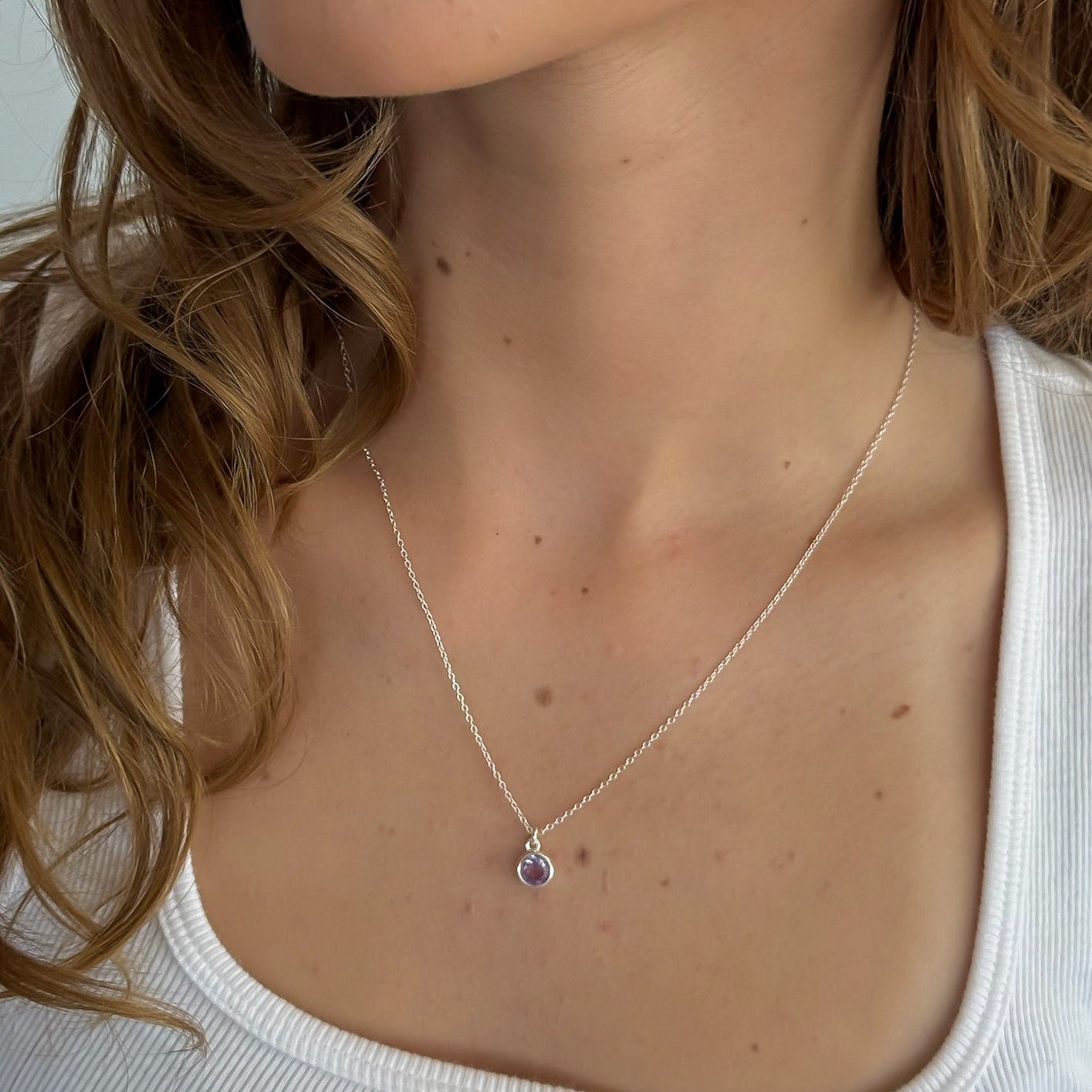 Necklace with a pendant worn by a person with light skin and brown hair.