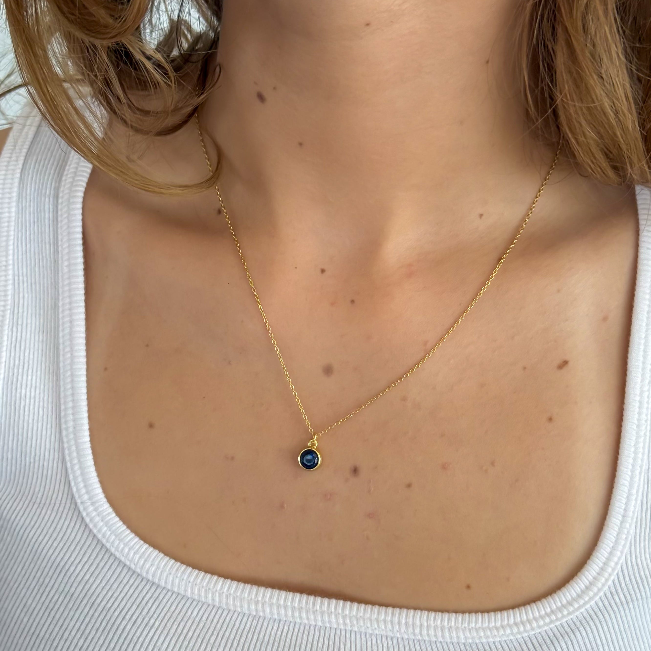 Gold necklace with a blue pendant on a person wearing a white tank top.