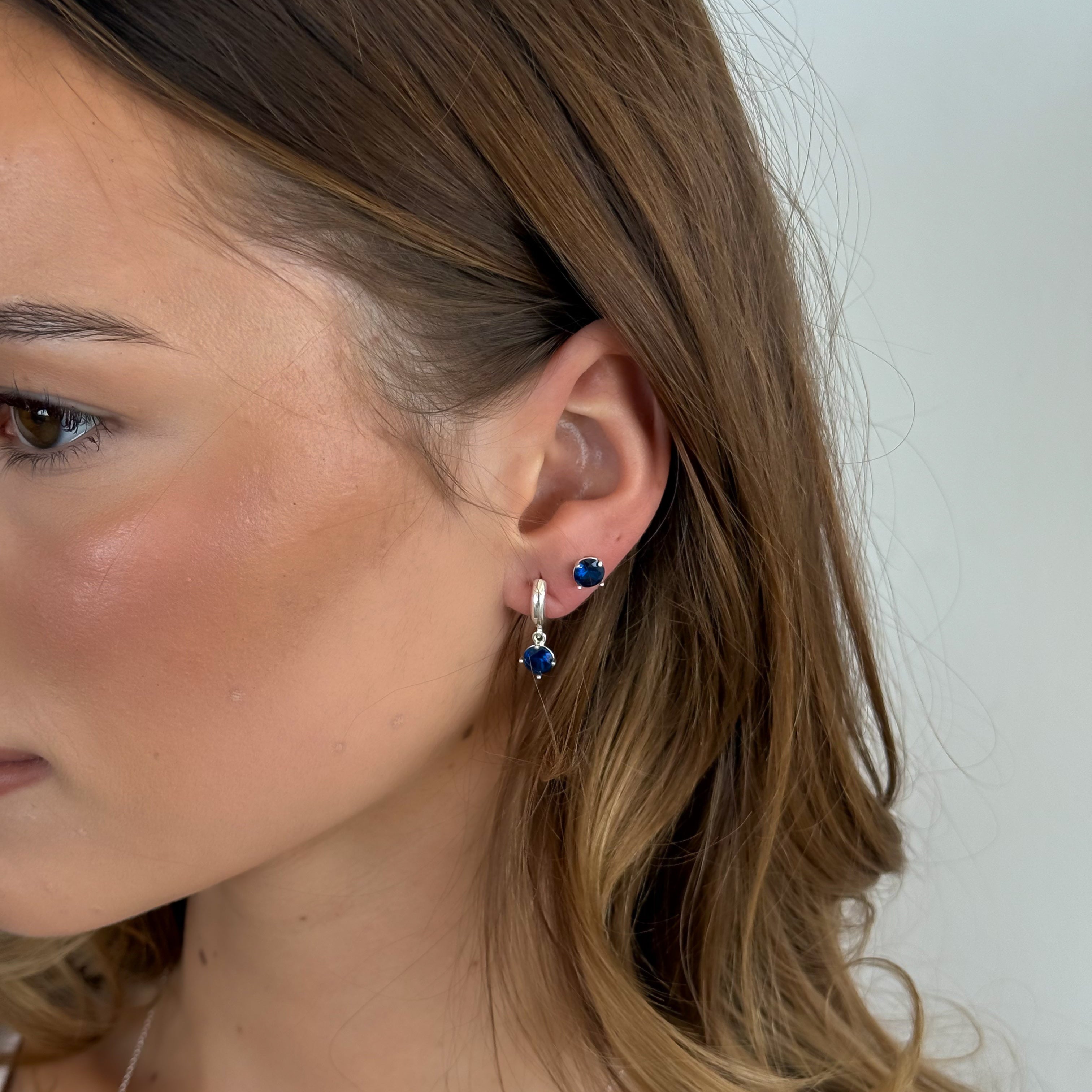 Close-up of a person wearing blue hoop earrings with a plain background