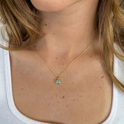 Close-up of a necklace with a pendant worn by a person in a white top.