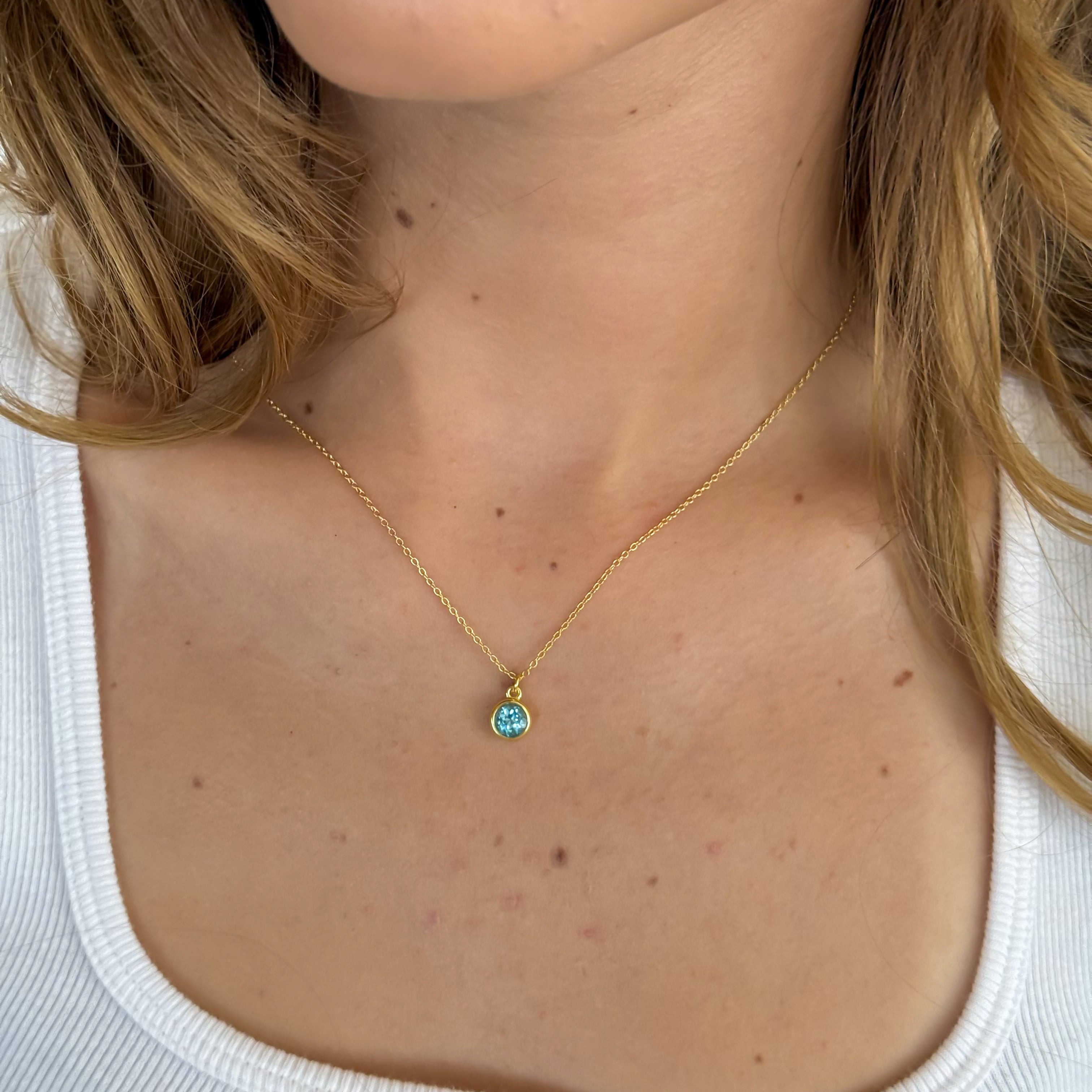 Close-up of a necklace with a pendant worn by a person in a white top.
