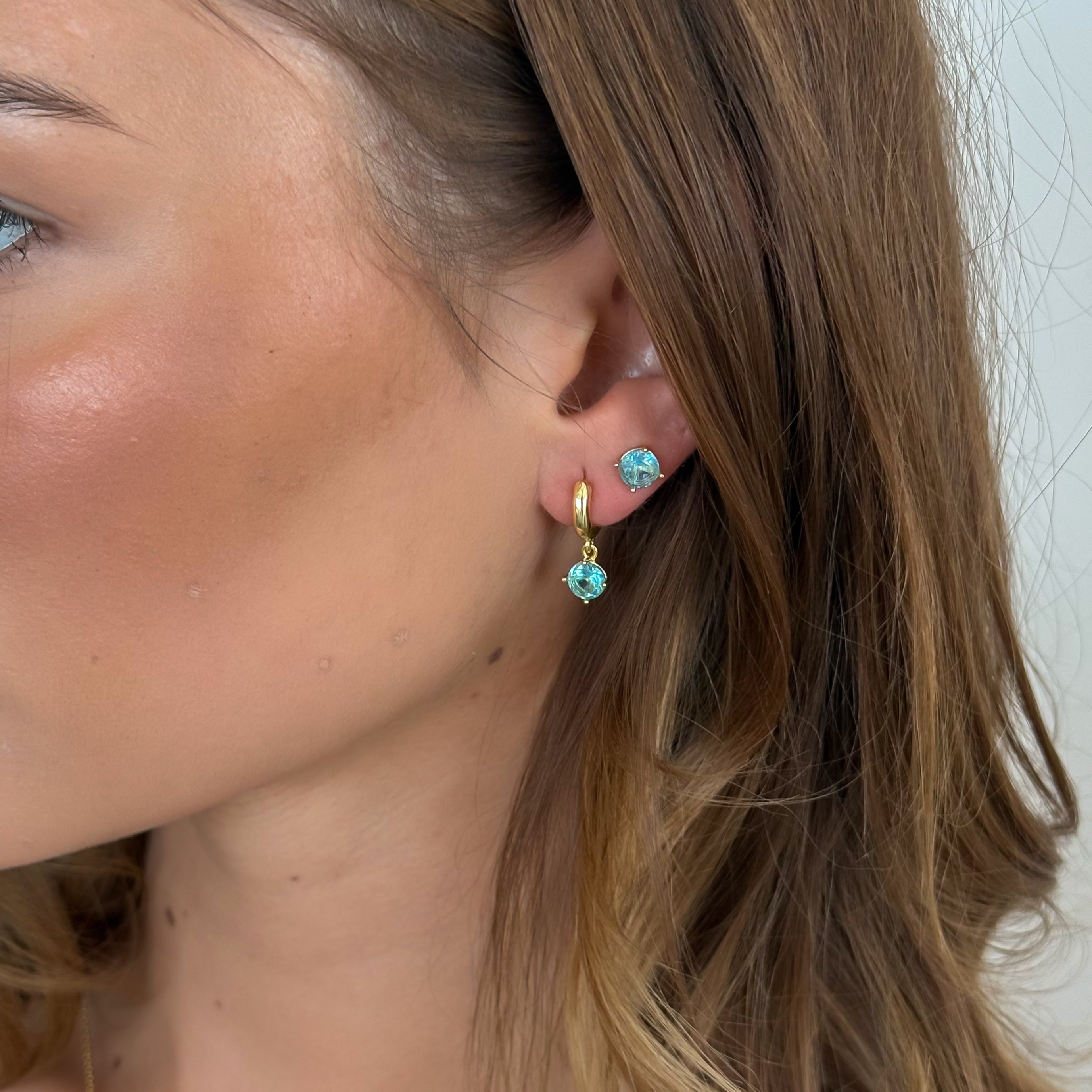 Close-up of a person wearing turquoise earrings with gold accents.