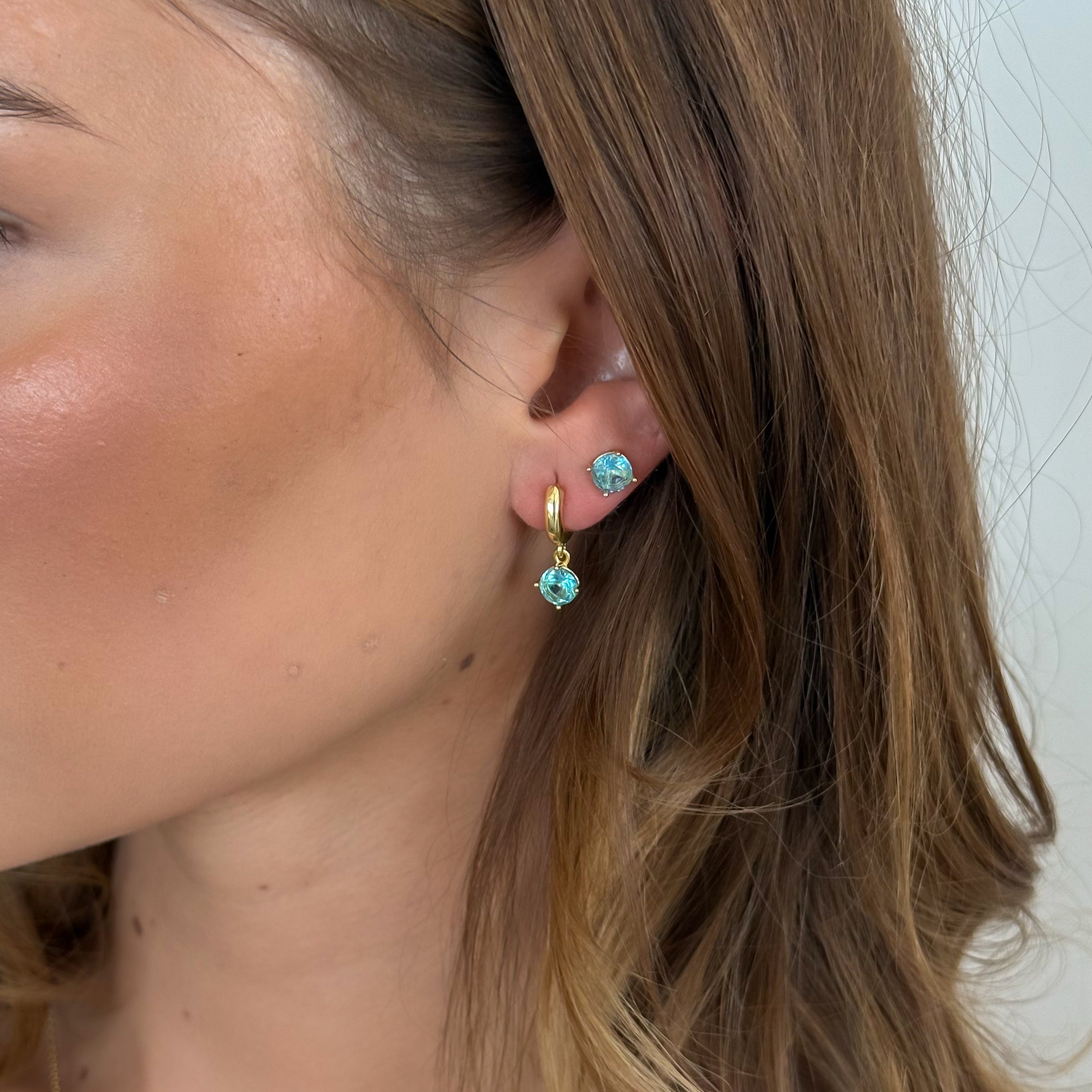 Close-up of a person wearing turquoise earrings with gold accents.
