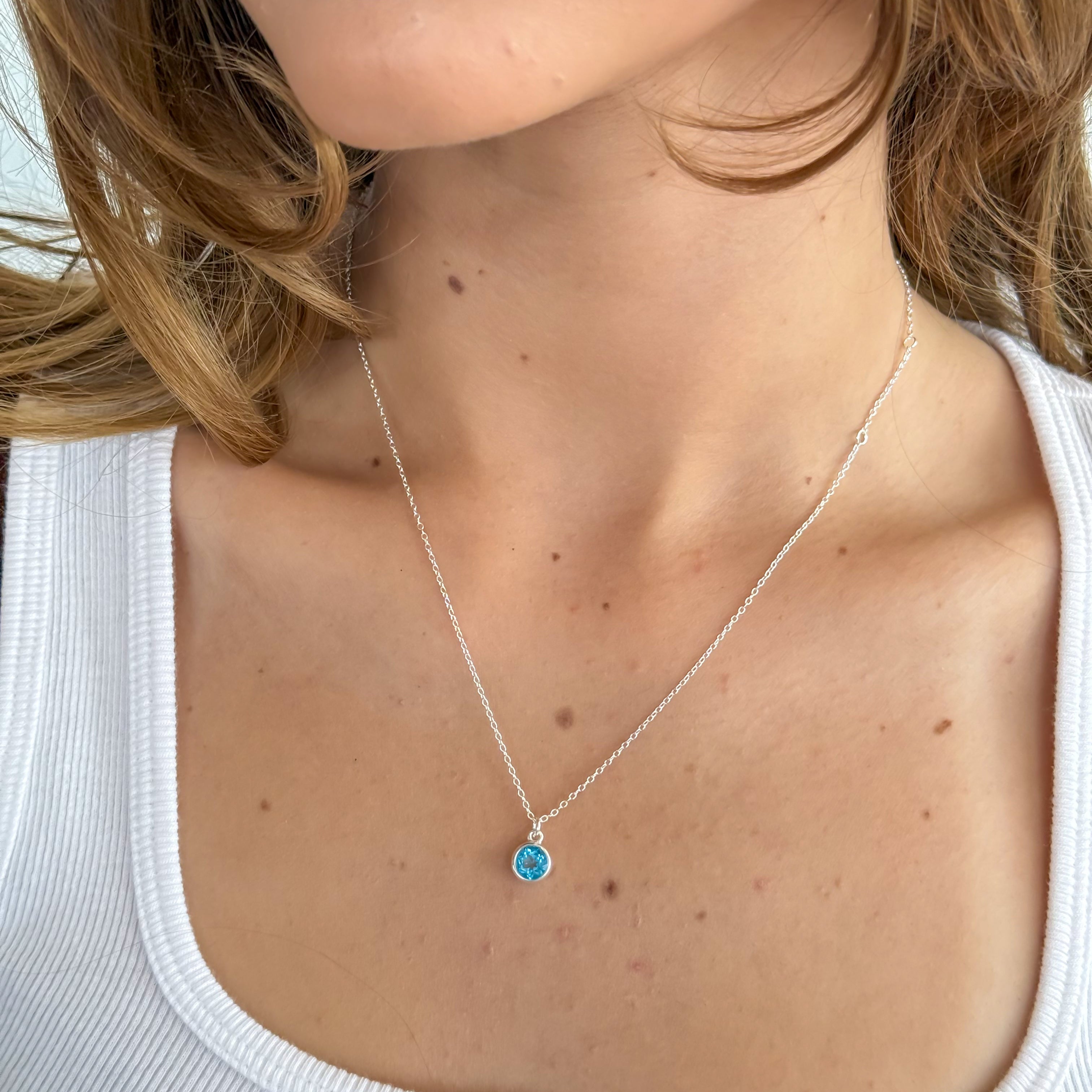 Necklace with a blue pendant worn by a person in a white tank top.