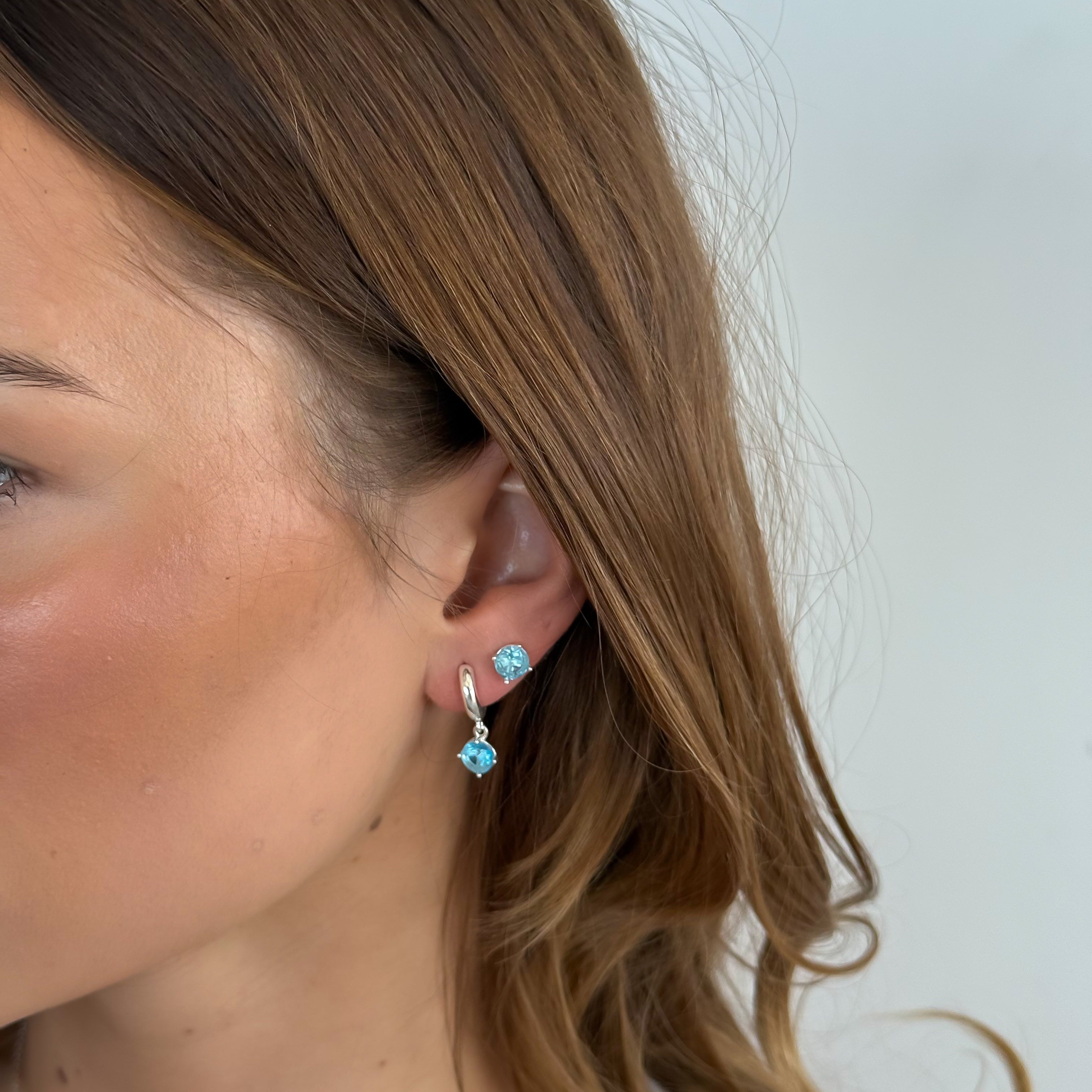 Close-up of a person wearing turquoise stud earrings with a plain background