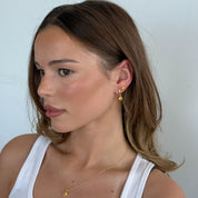 Woman wearing gold earrings and a necklace against a light background