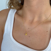Close-up of a person wearing a gold necklace with a yellow pendant against a light background