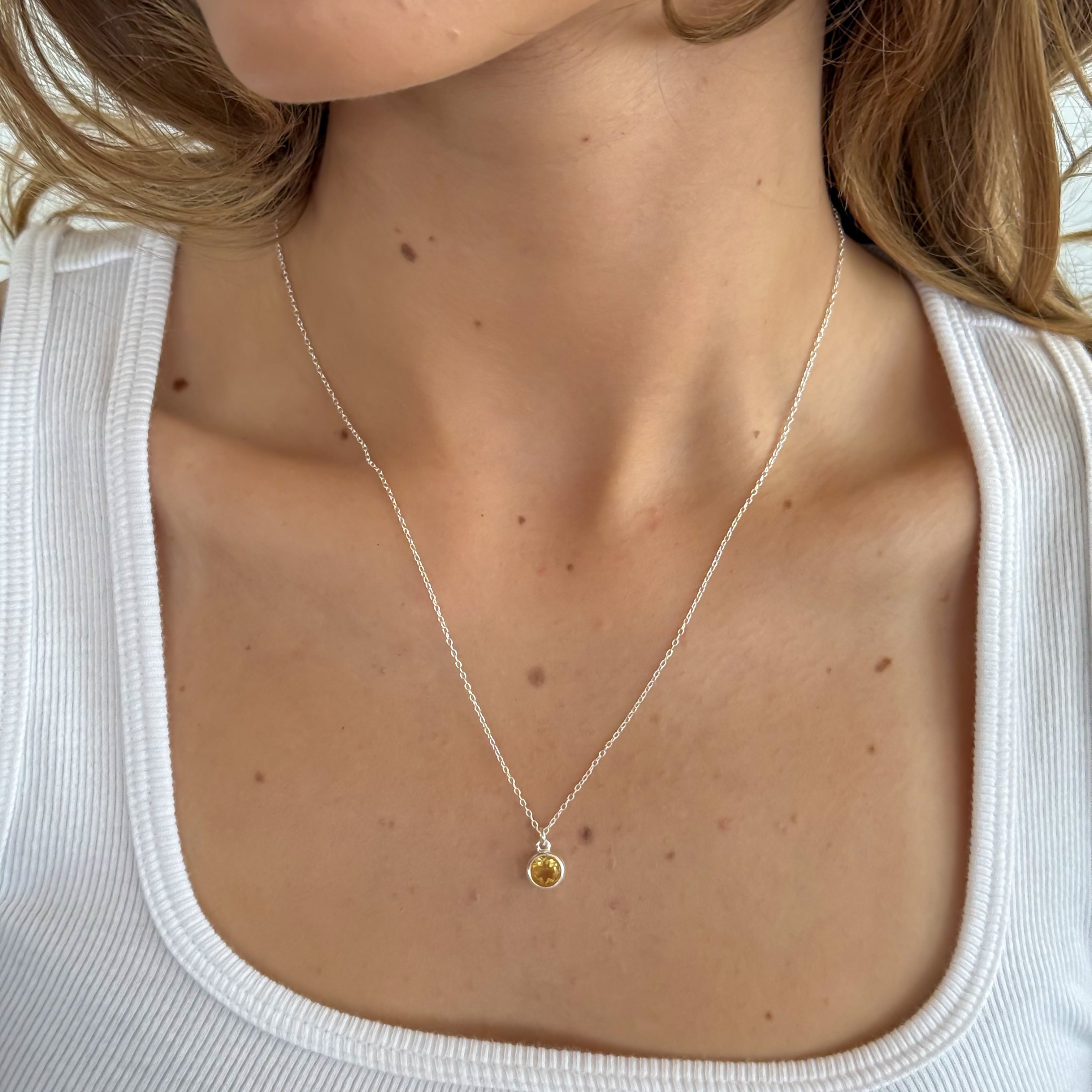 Necklace with a small pendant worn by a person in a white top