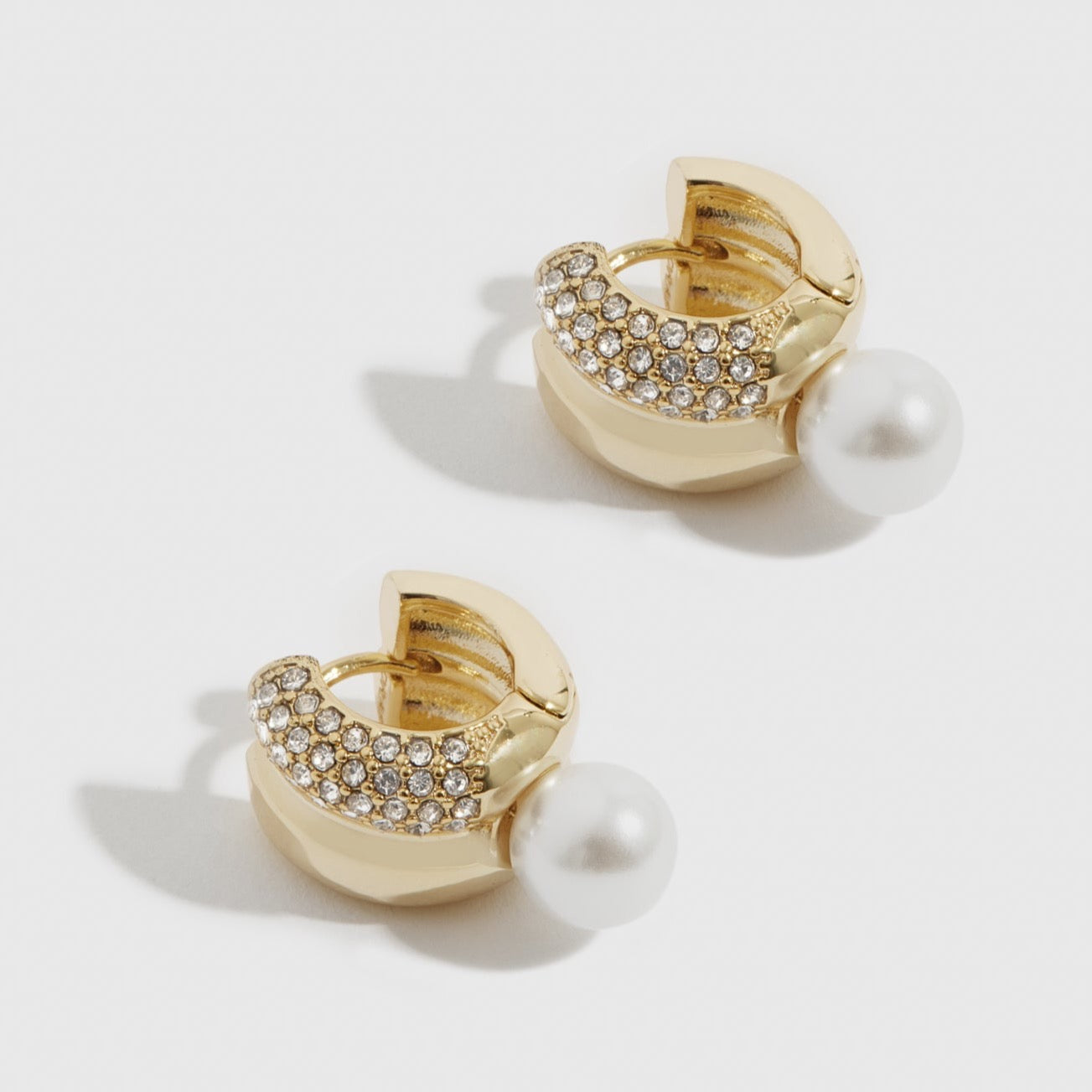 14k gold plated Vega huggie earrings with a pearl, shown on a plain background.