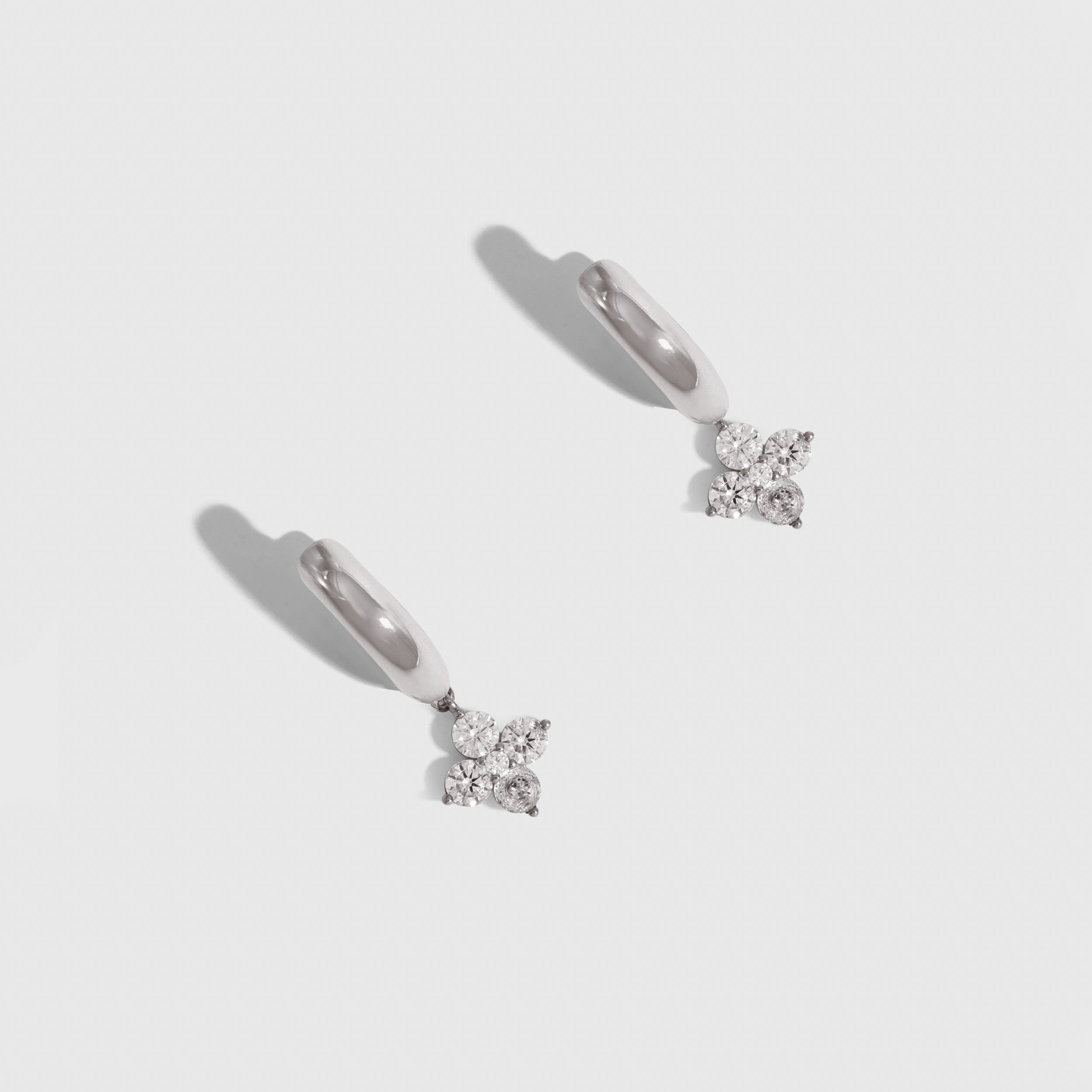 Silver clover motif huggie hoop earrings with cubic zirconia detailing, shown on a plain background.