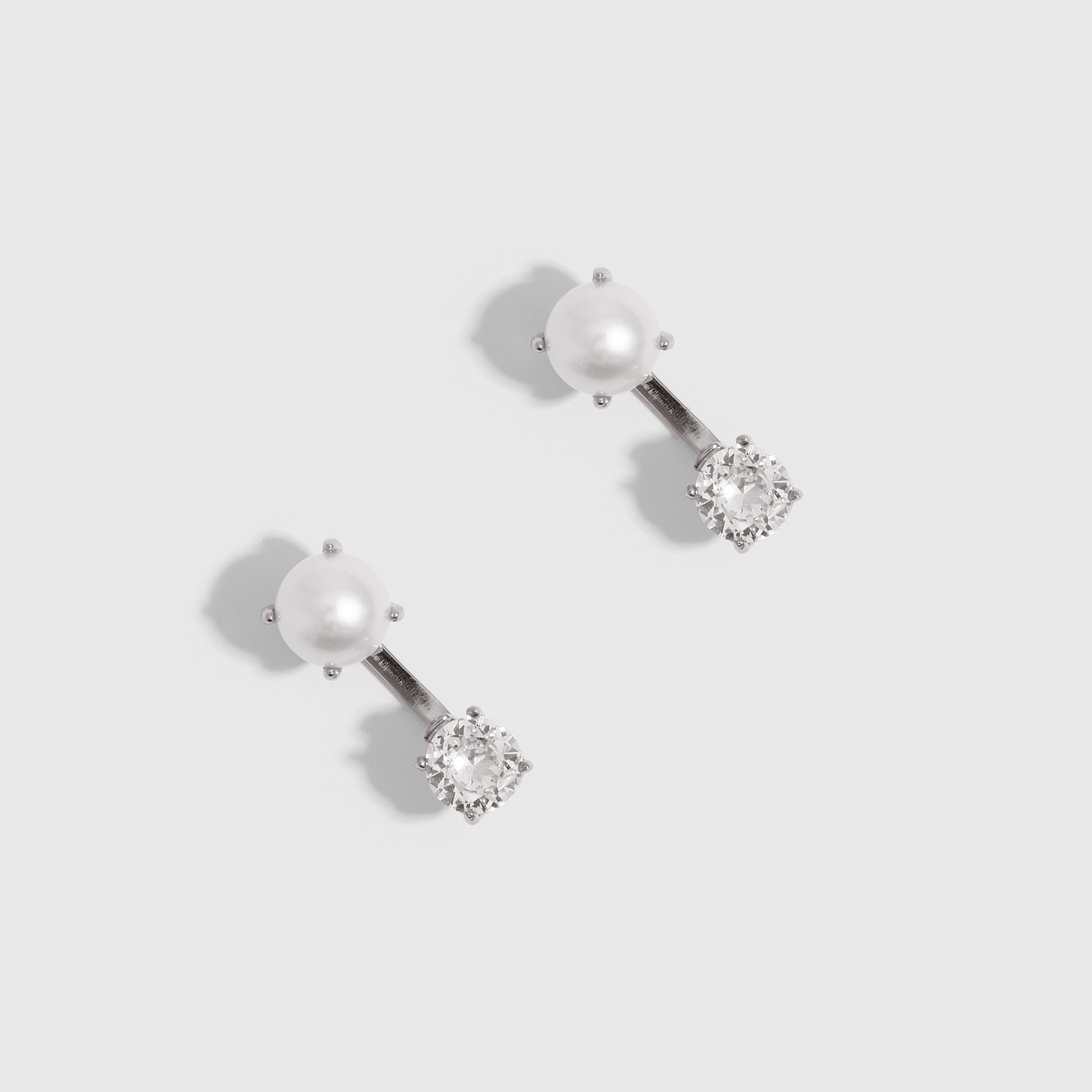 Silver barbell earrings combining a freshwater pearl and a round-cut cubic zirconia, shown on a plain background.