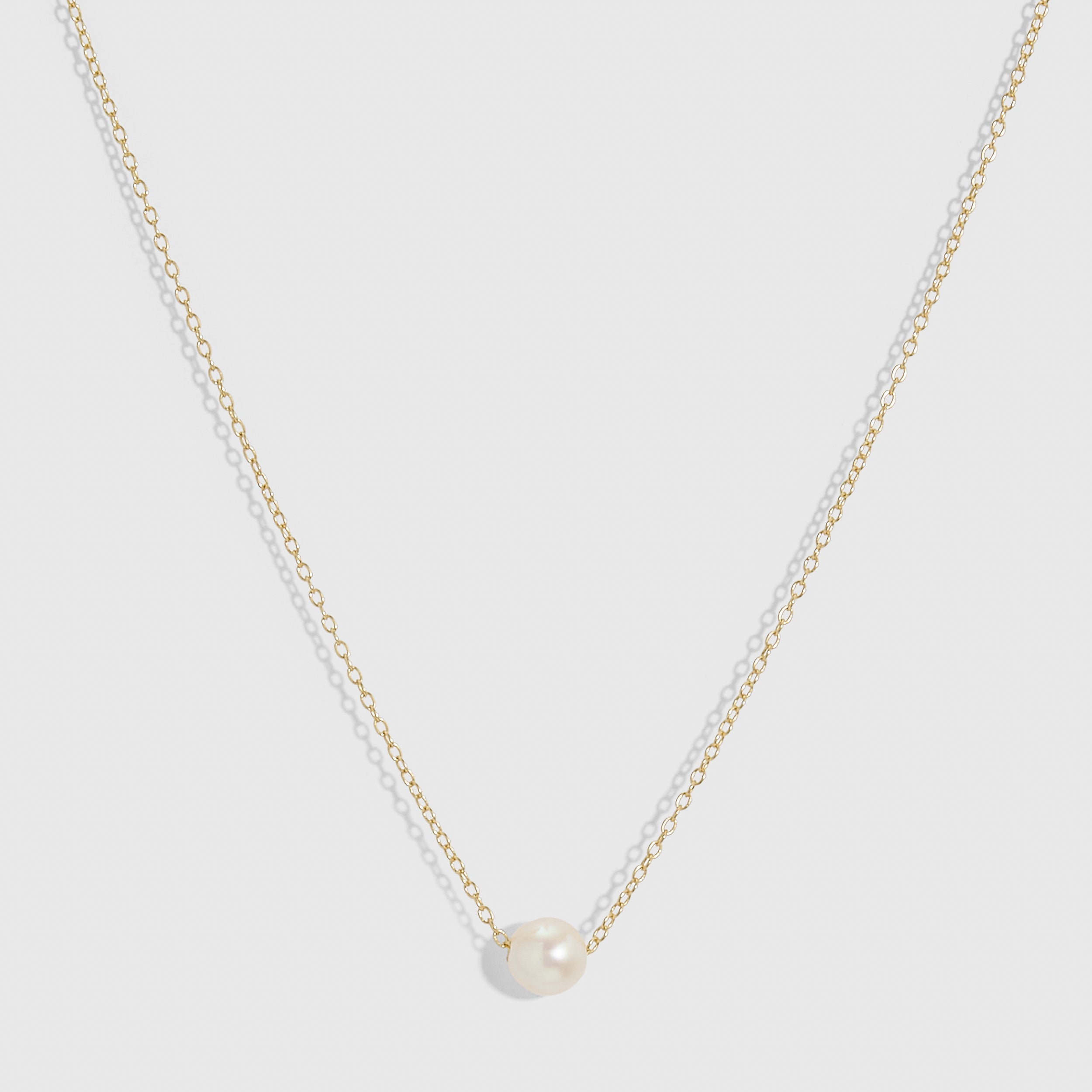 14k gold plated solitaire pendant necklace with one round freshwater pearl on a fine cable chain, shown on a plain background.