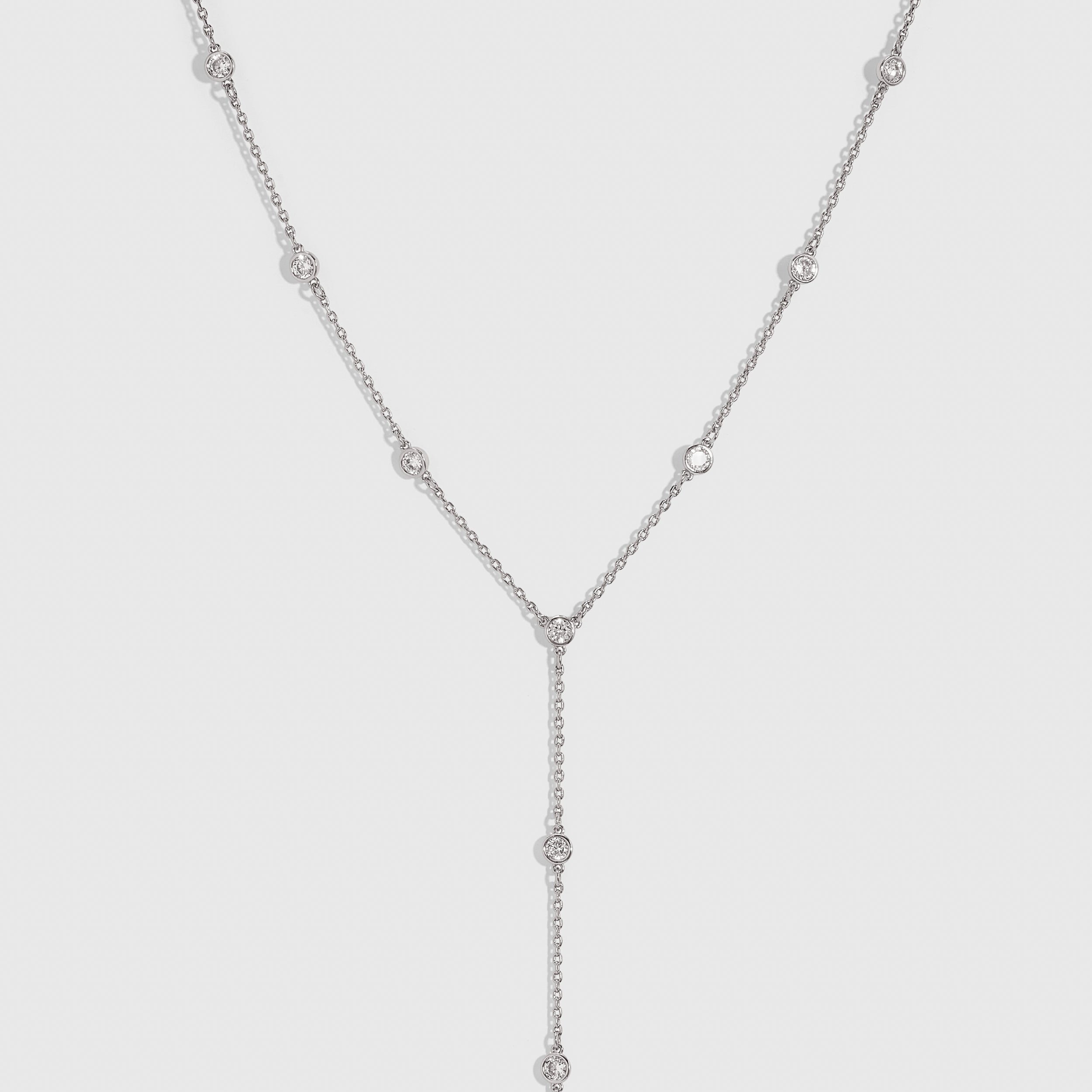 Silver bezel-set cubic zirconia lariat necklace with a draped adjustable chain, shown on a plain background.
