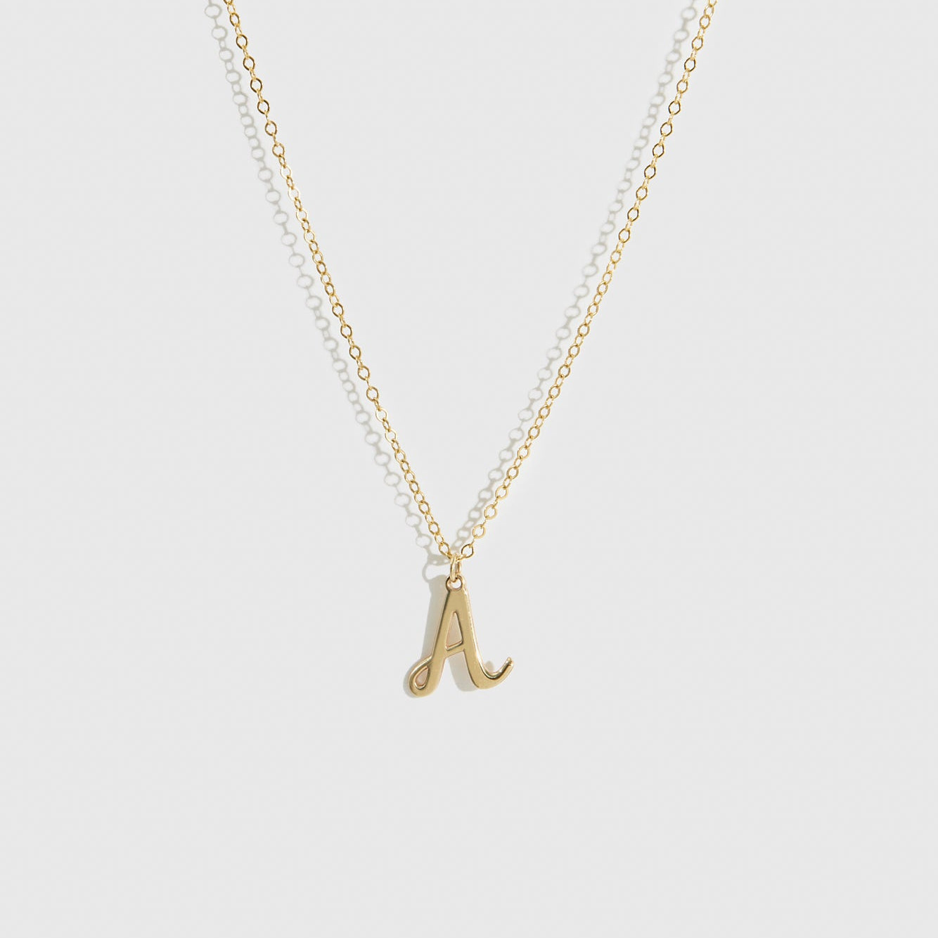 14k solid gold cursive font letter pendant necklace, shown on a plain background.