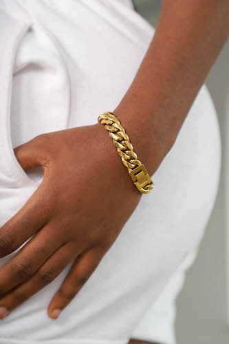 Dark skinned young woman in white sweatpants and hand in pocket wearing beautiful gold bracelet from Drae jewelry collection