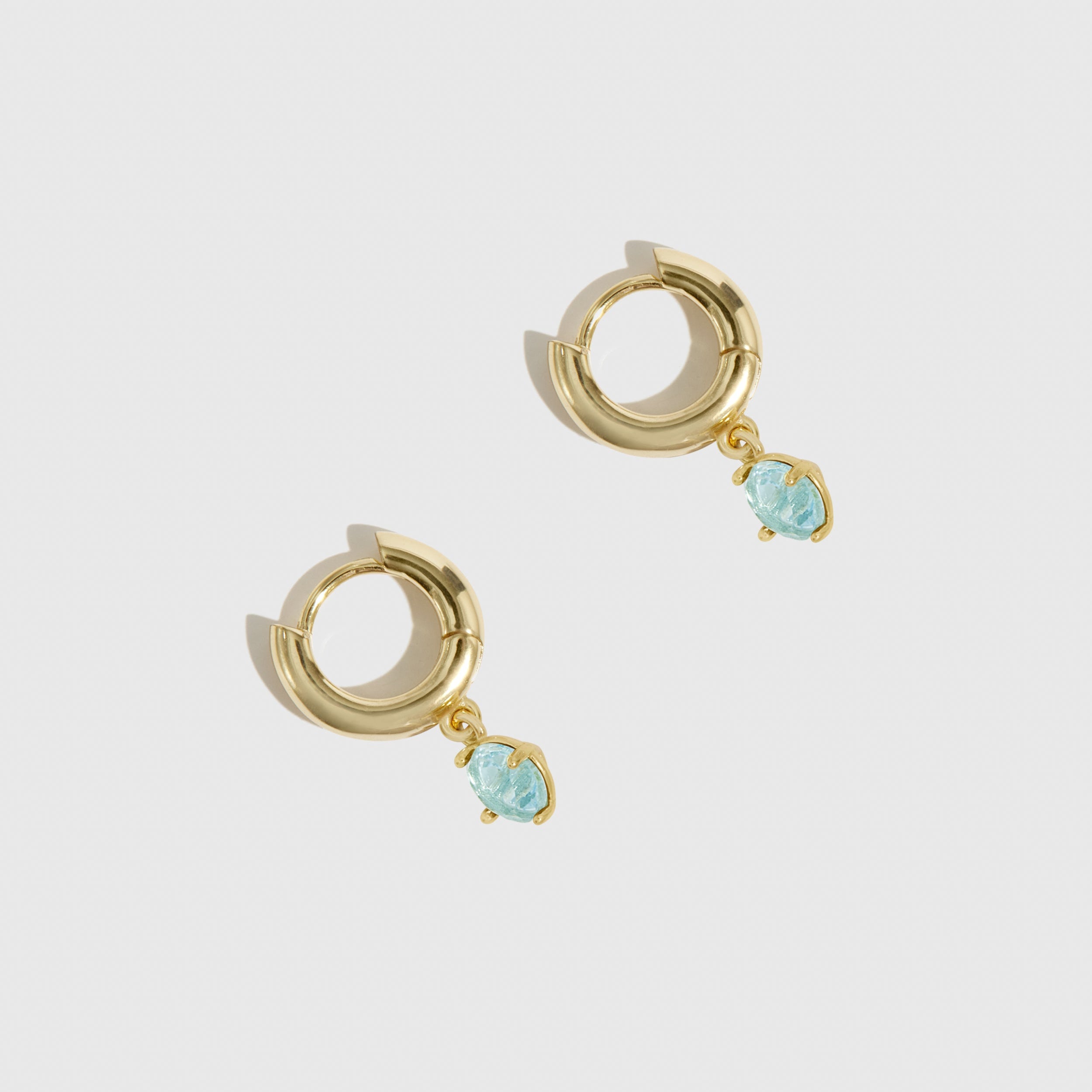 Gold hoop earrings with turquoise stones on a light gray background