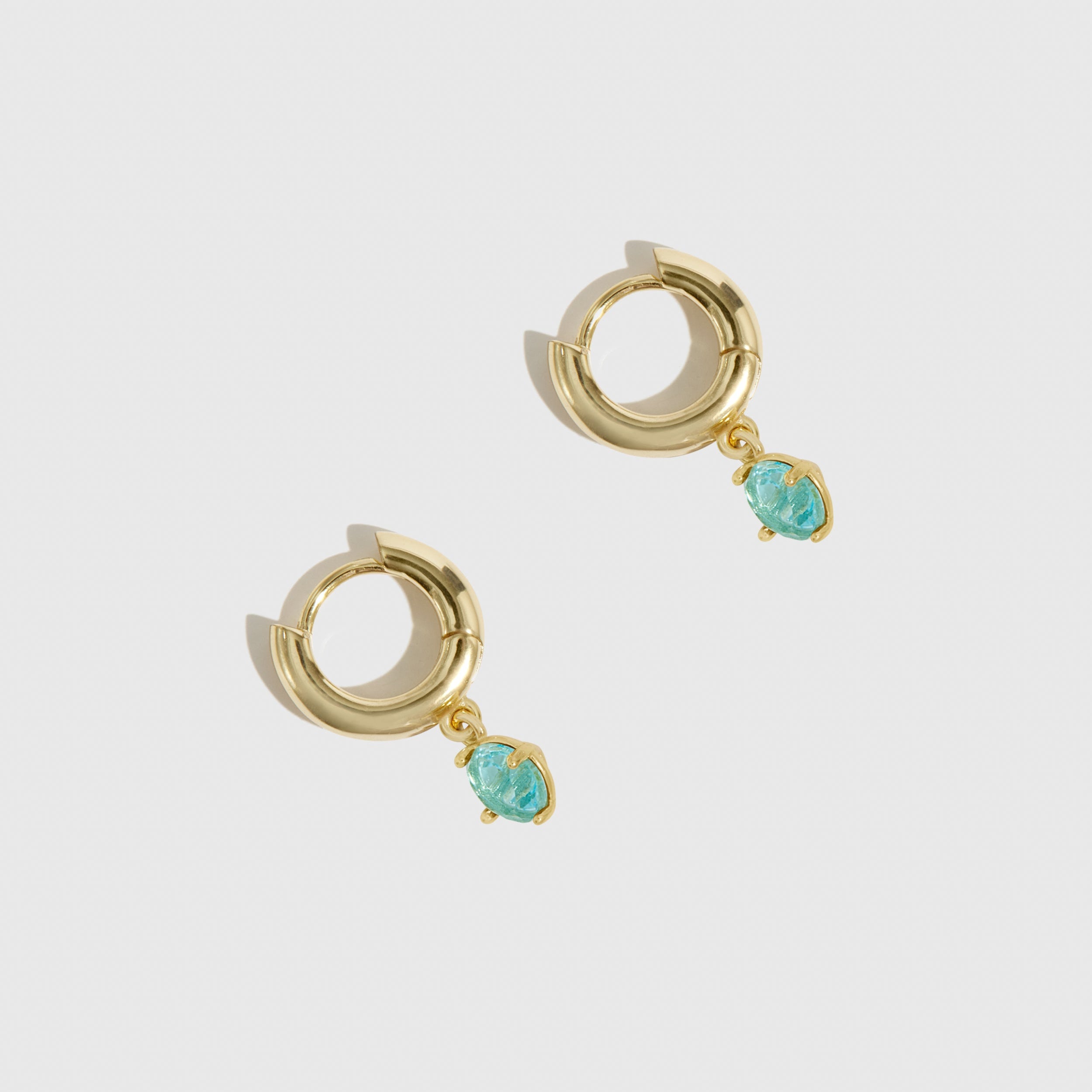 Gold hoop earrings with turquoise stones on a light gray background