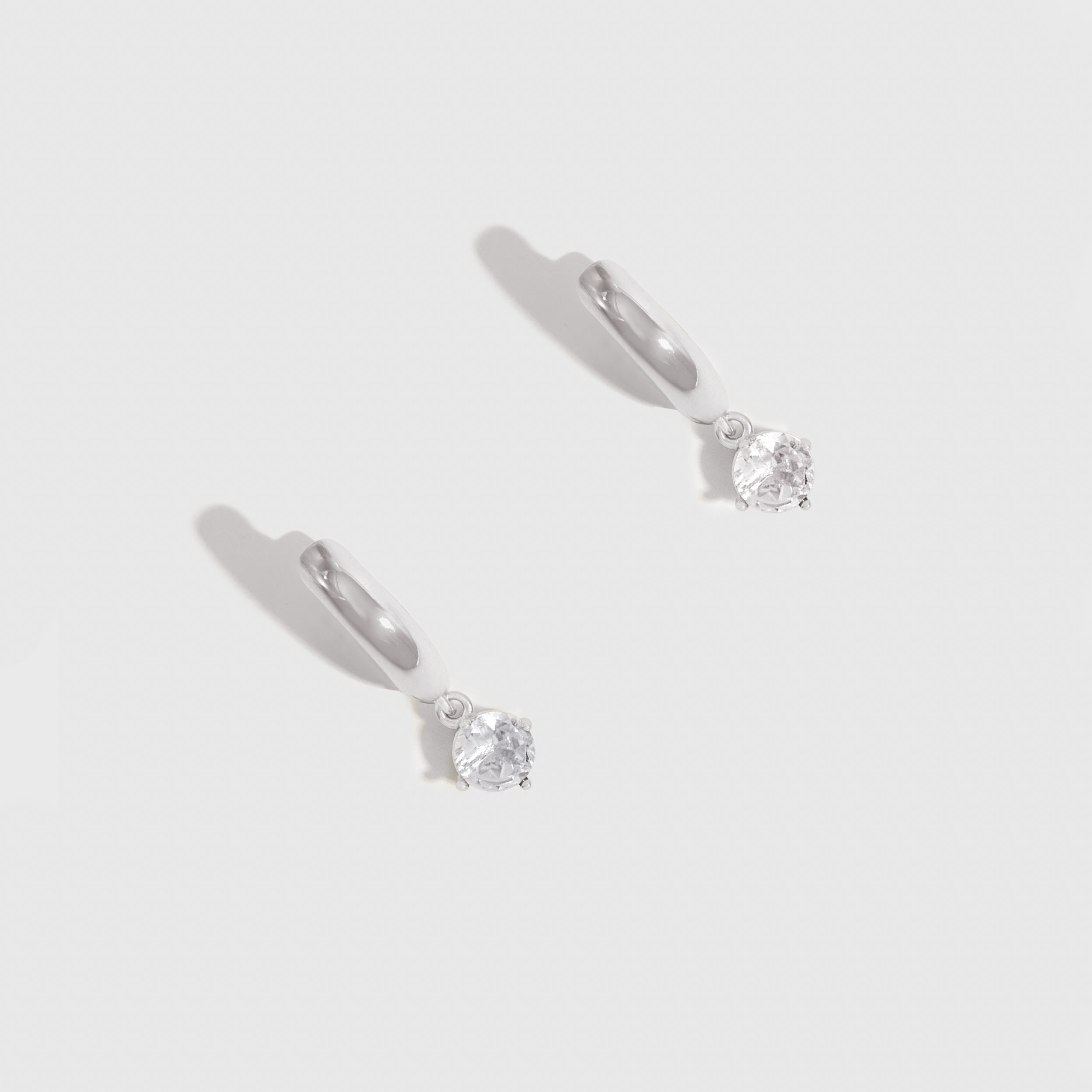 Pair of silver stud earrings with clear gemstones on a light gray background
