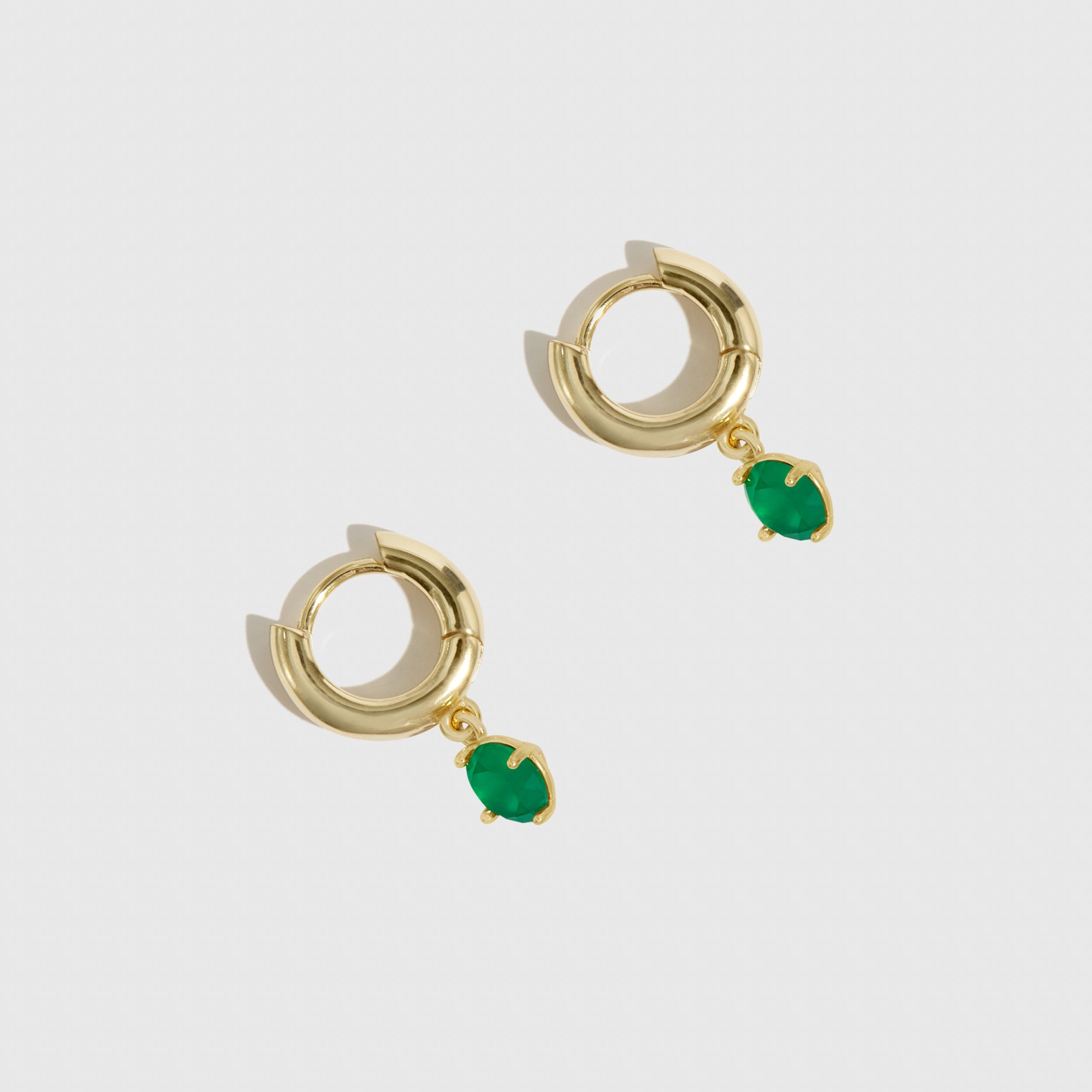 Gold hoop earrings with green gemstones on a light gray background