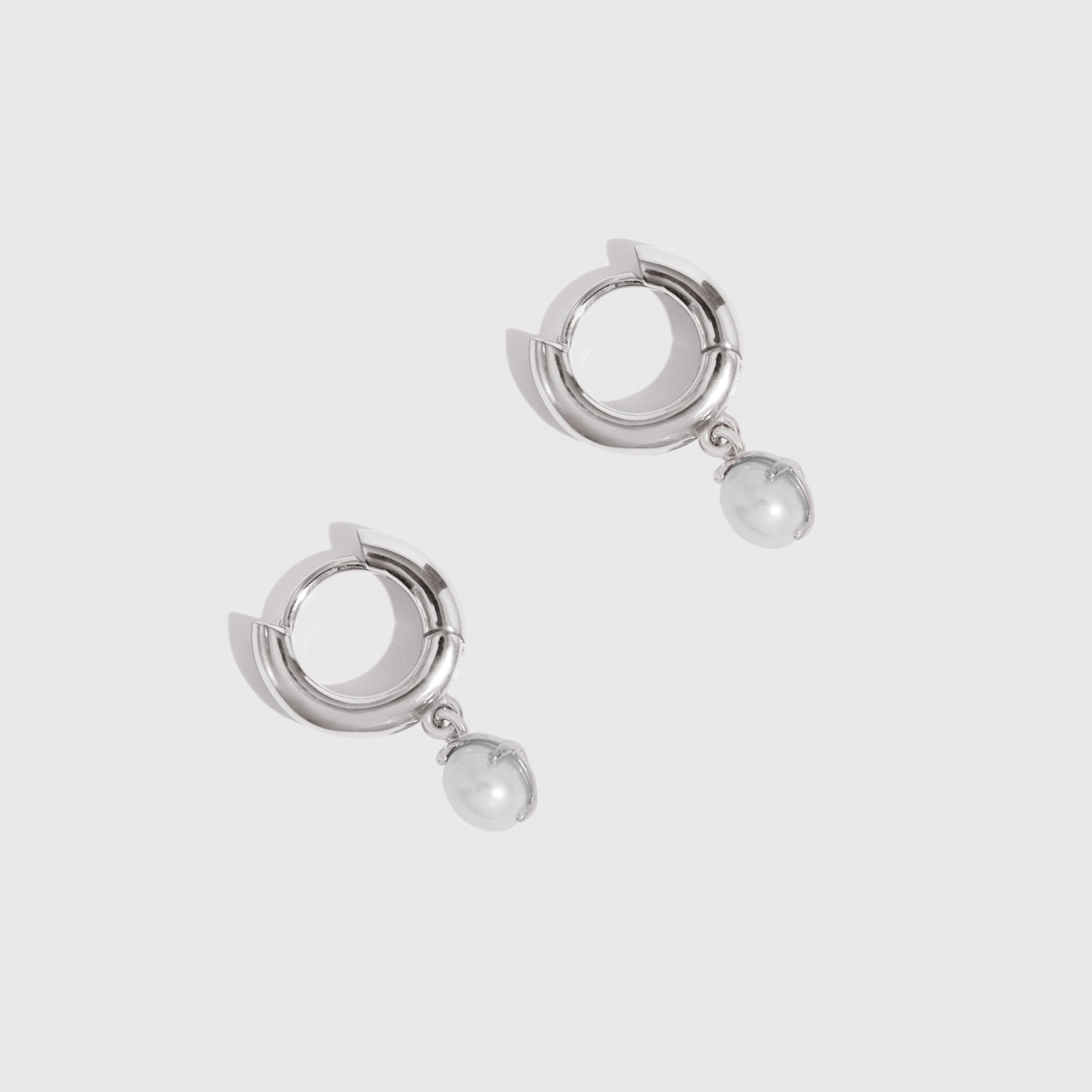 Pair of silver hoop earrings with pearl drops on a light gray background