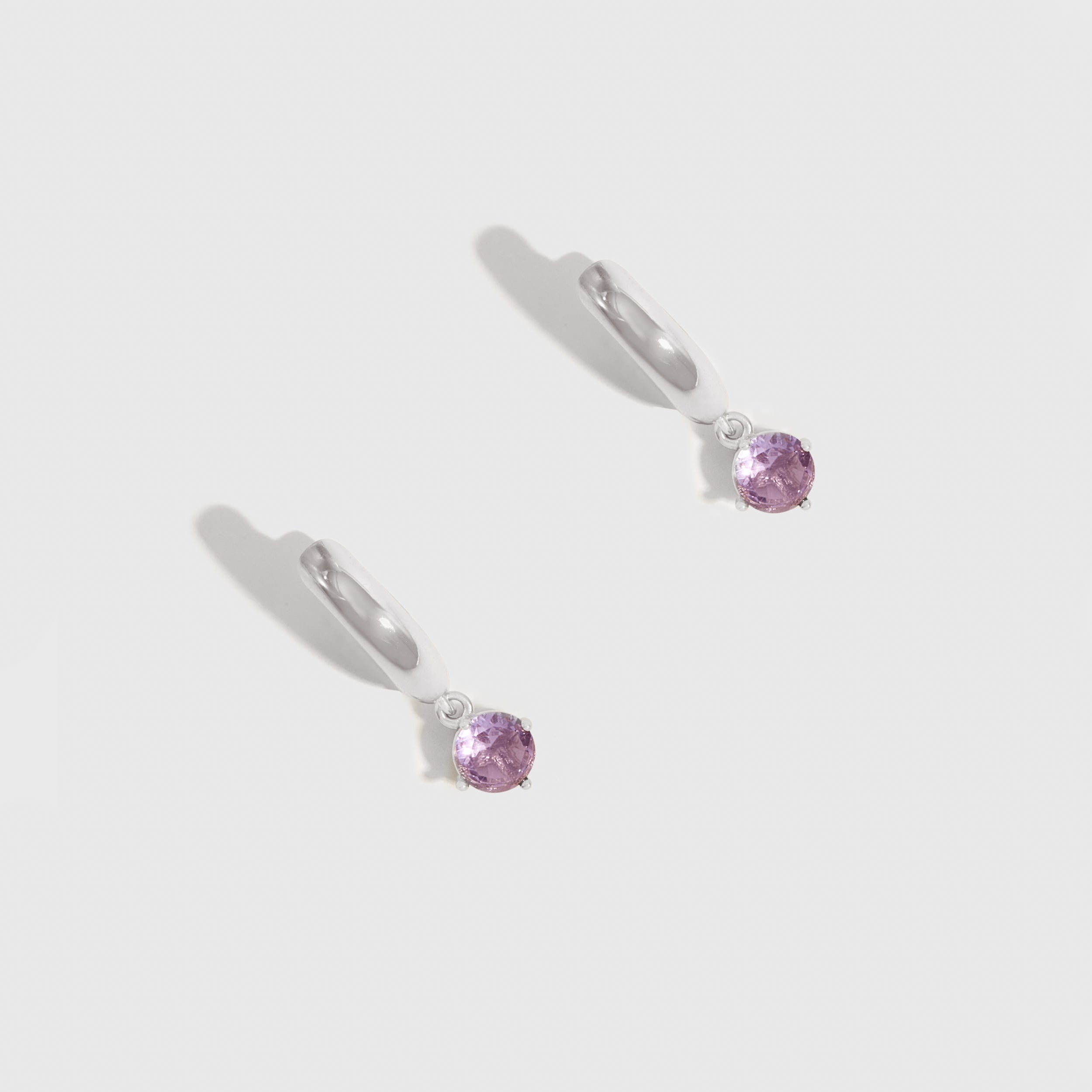 Pair of silver earrings with purple gemstones on a light gray background