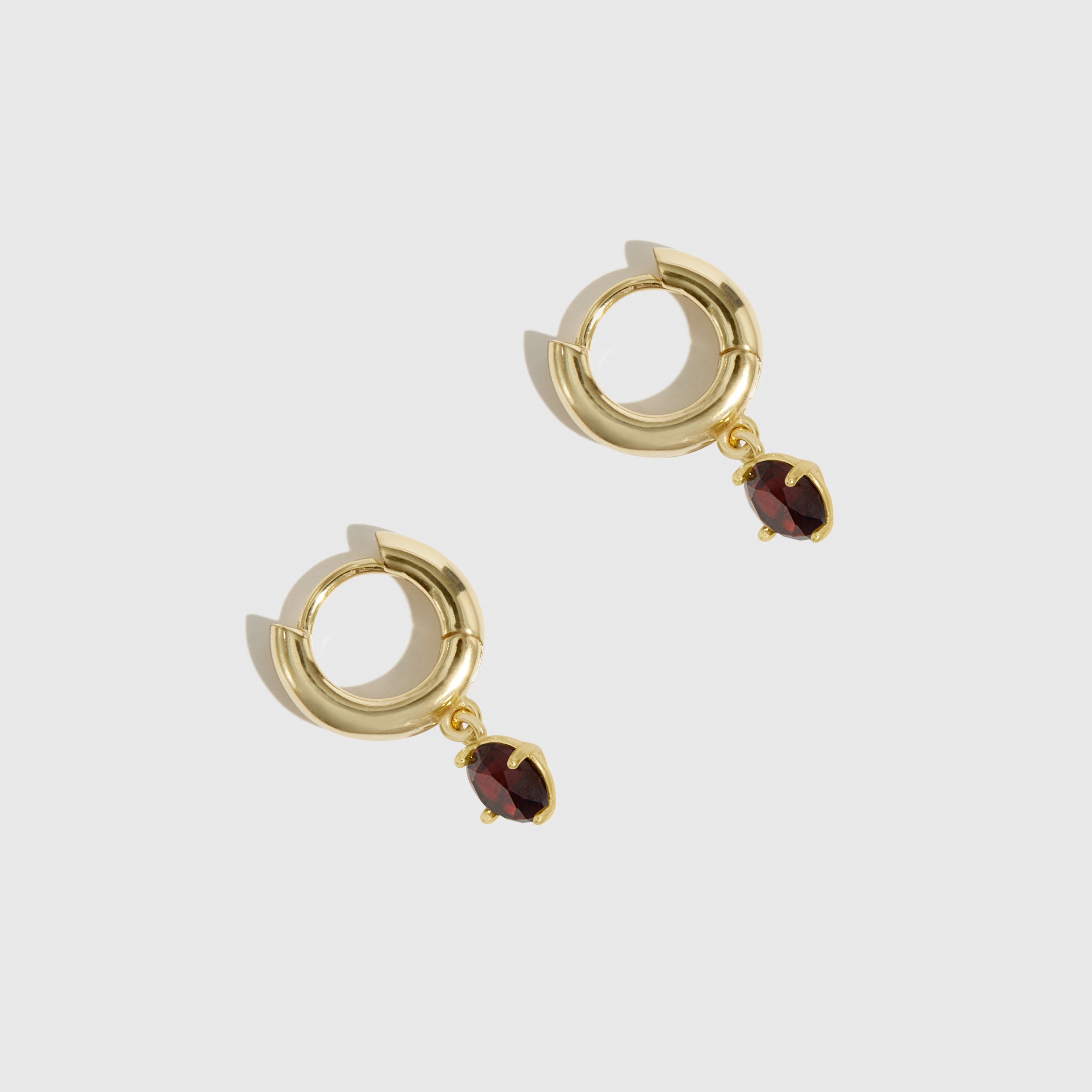 Gold hoop earrings with red gemstones on a white background