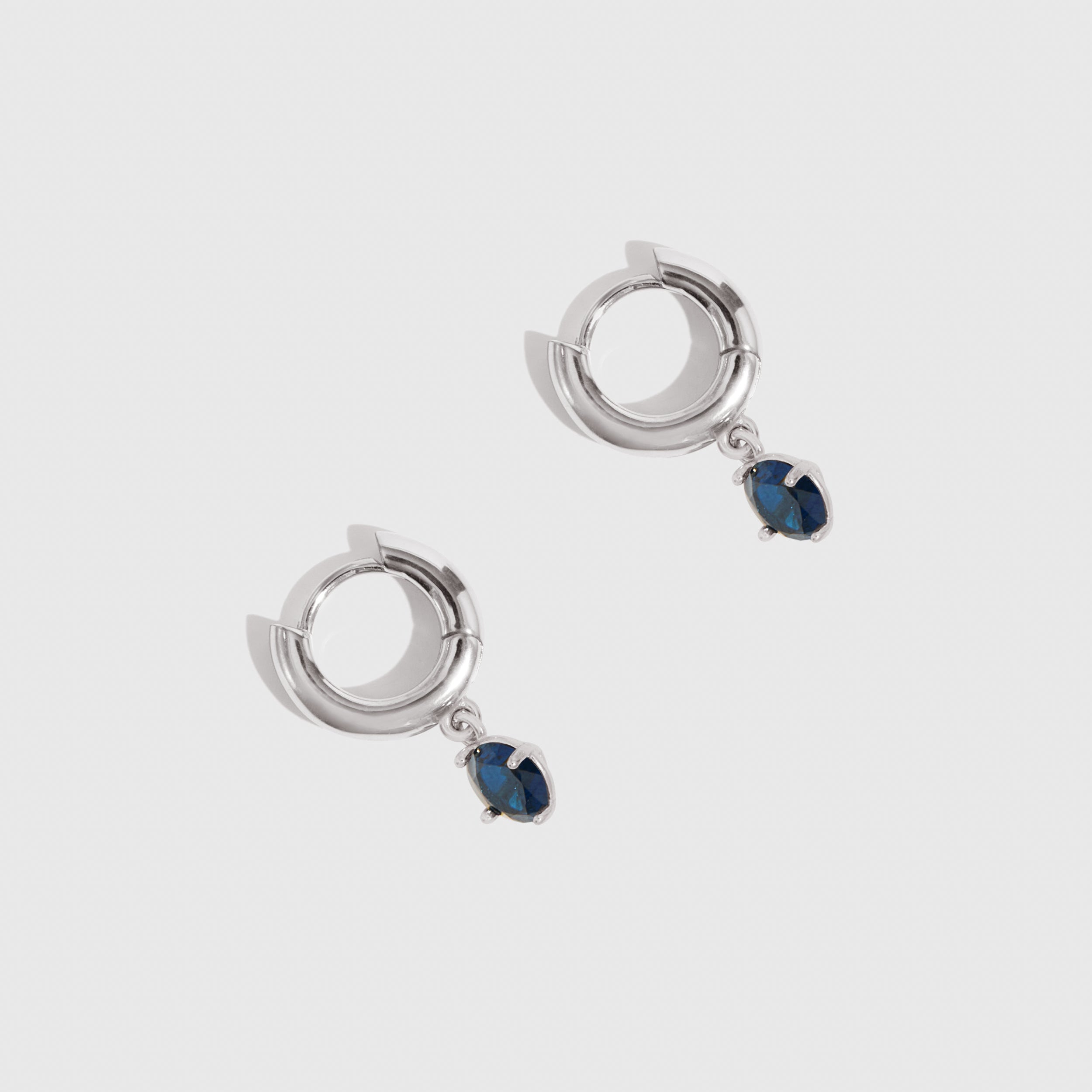 Pair of silver hoop earrings with blue gemstones on a white background