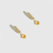 Gold earrings with yellow gemstones on a light gray background