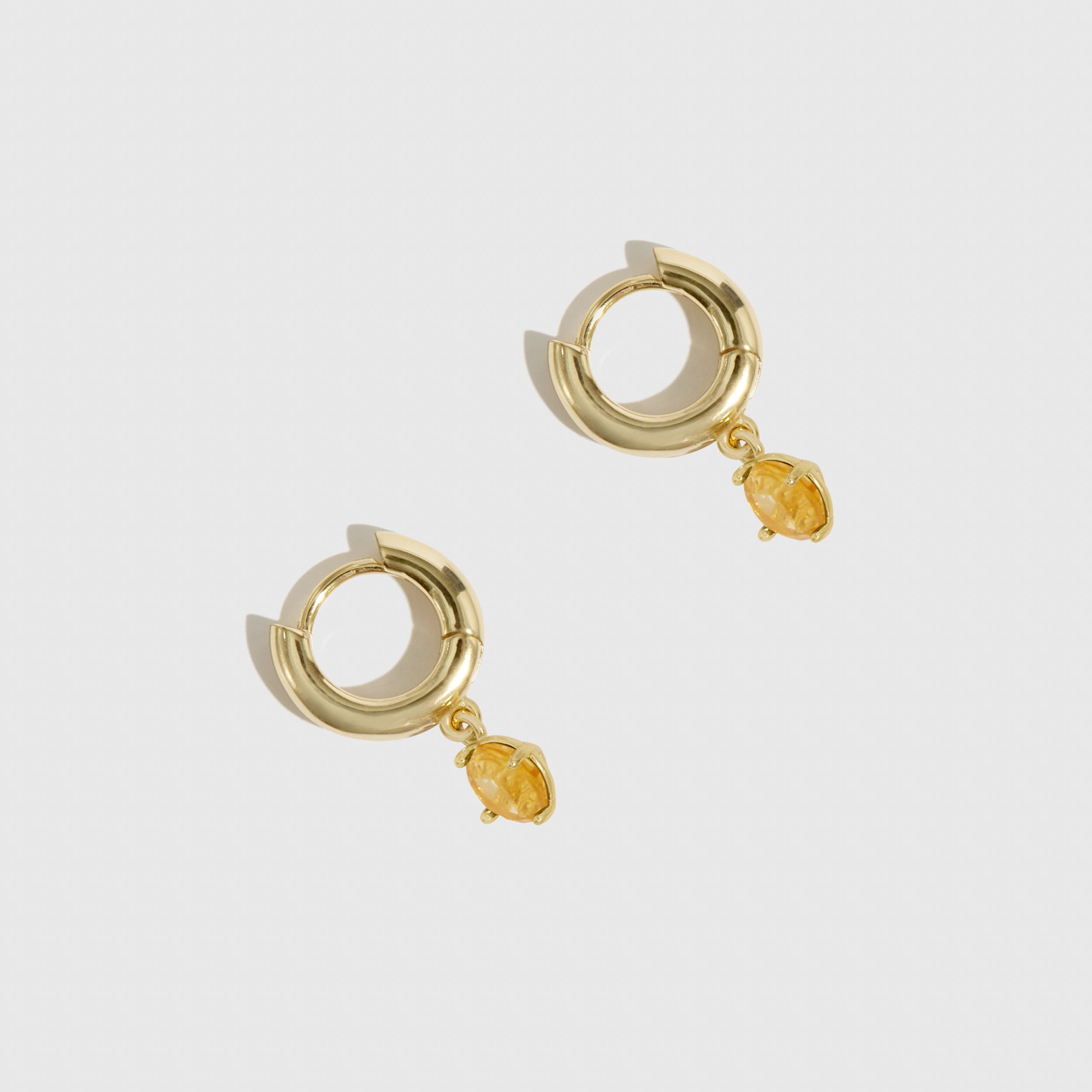 Gold hoop earrings with small yellow gemstones on a light gray background