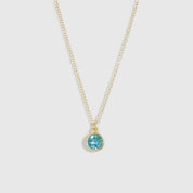 Gold necklace with a blue gemstone pendant on a light gray background