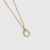 Gold necklace with a clear gemstone pendant on a light gray background