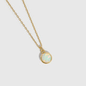 Gold necklace with a round opal pendant on a light gray background