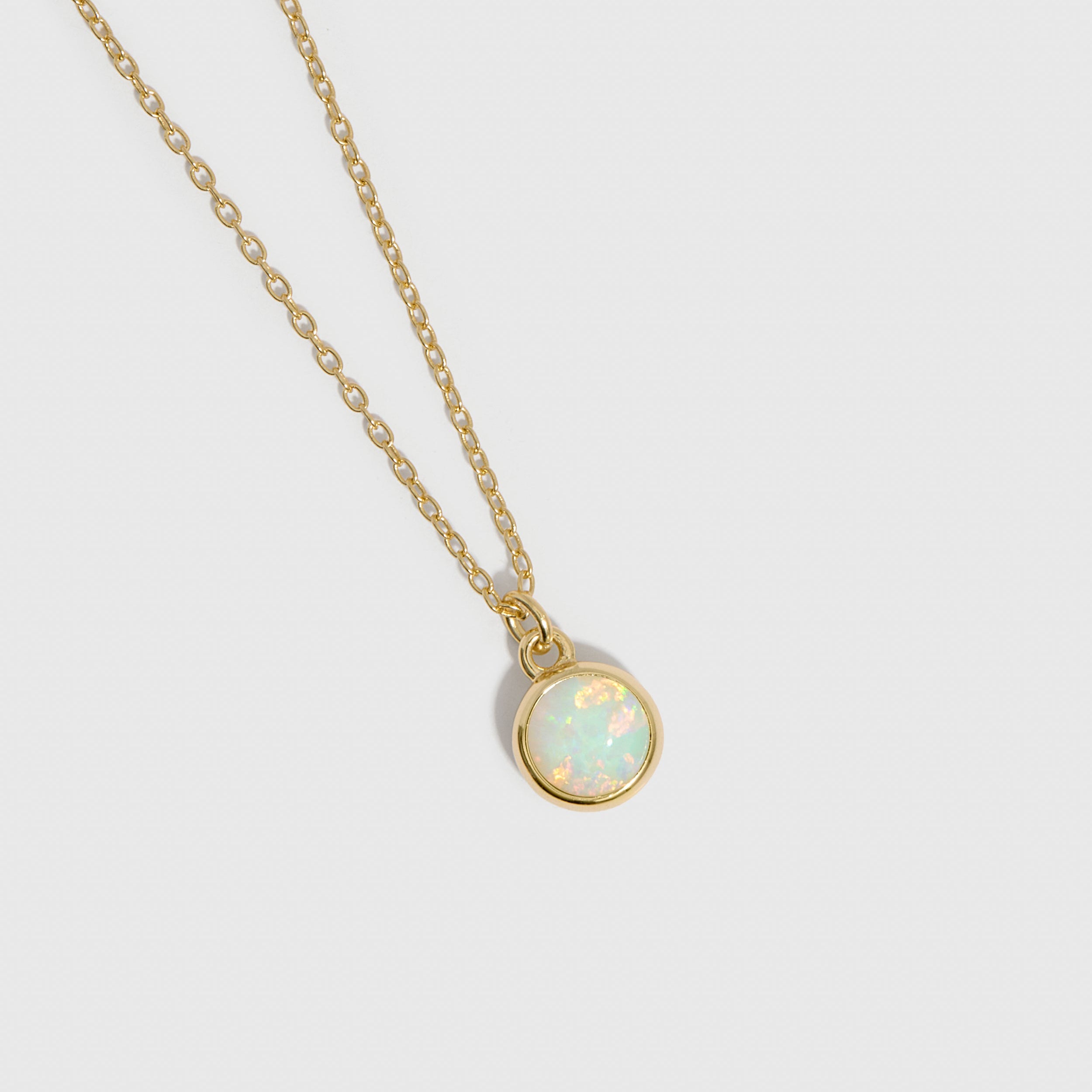 Gold necklace with a round opal pendant on a light gray background