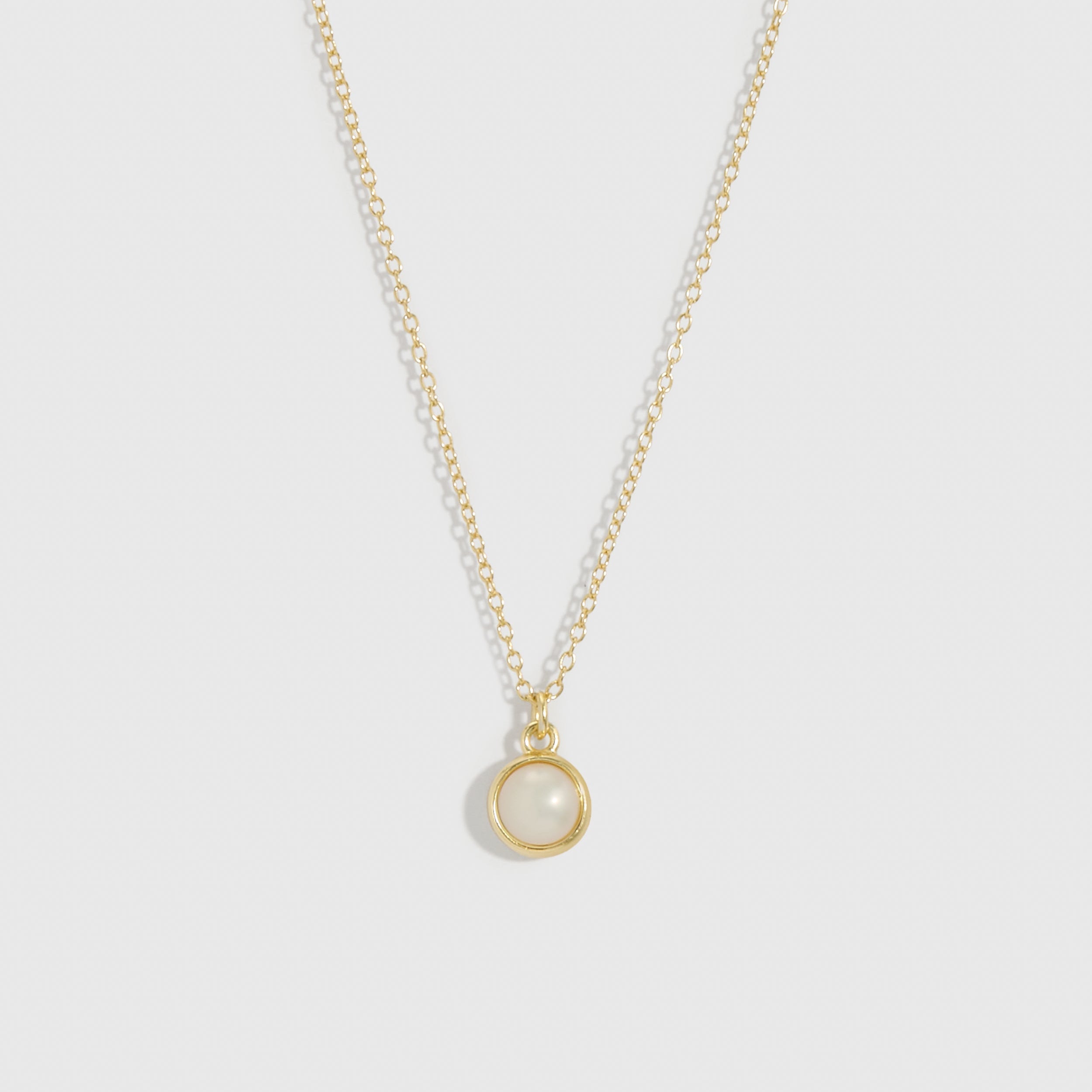 Gold necklace with a round pendant on a light gray background