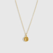 Gold necklace with a round pendant on a light gray background