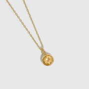 Gold necklace with a round pendant on a light gray background