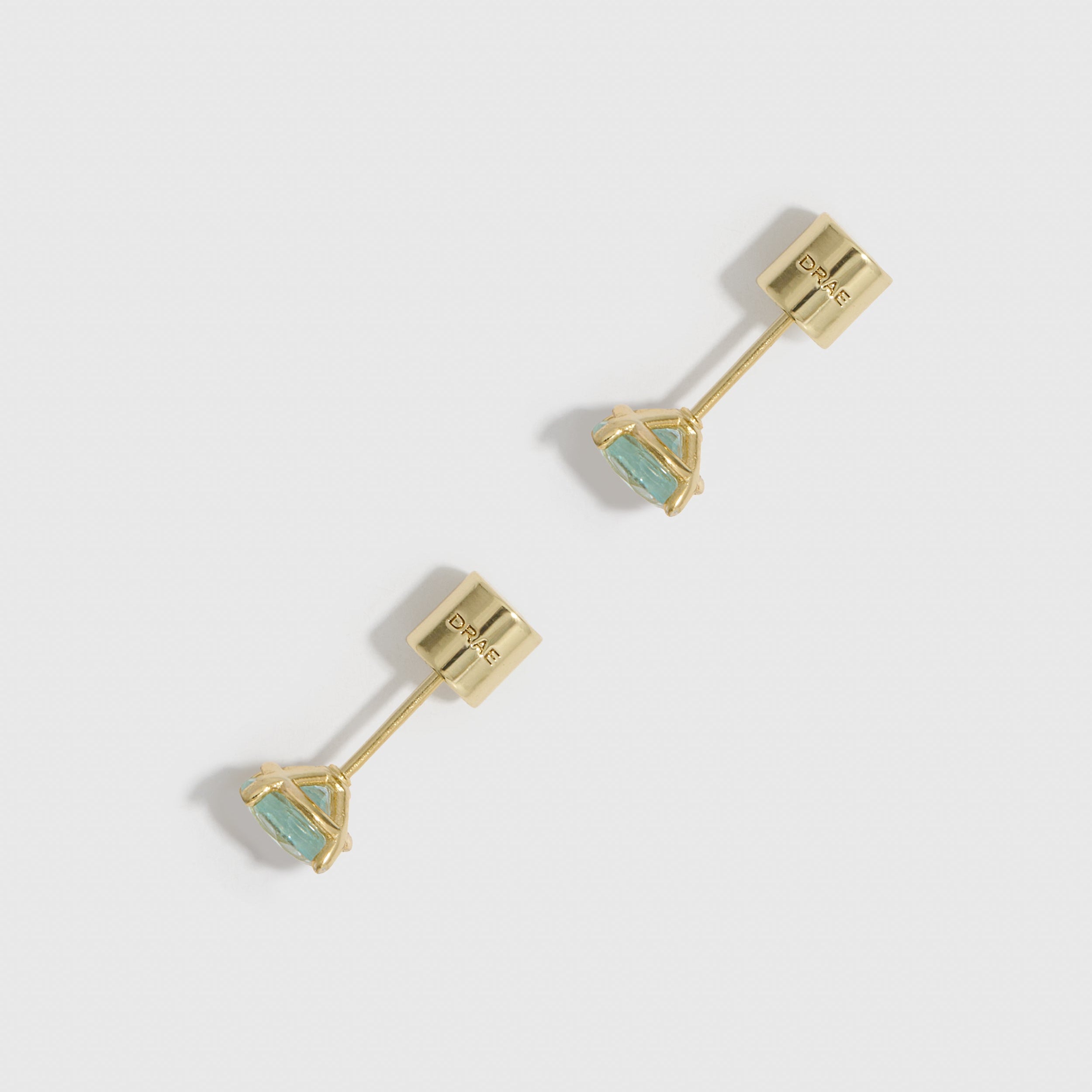 Gold earrings with triangular gemstones on a light gray background