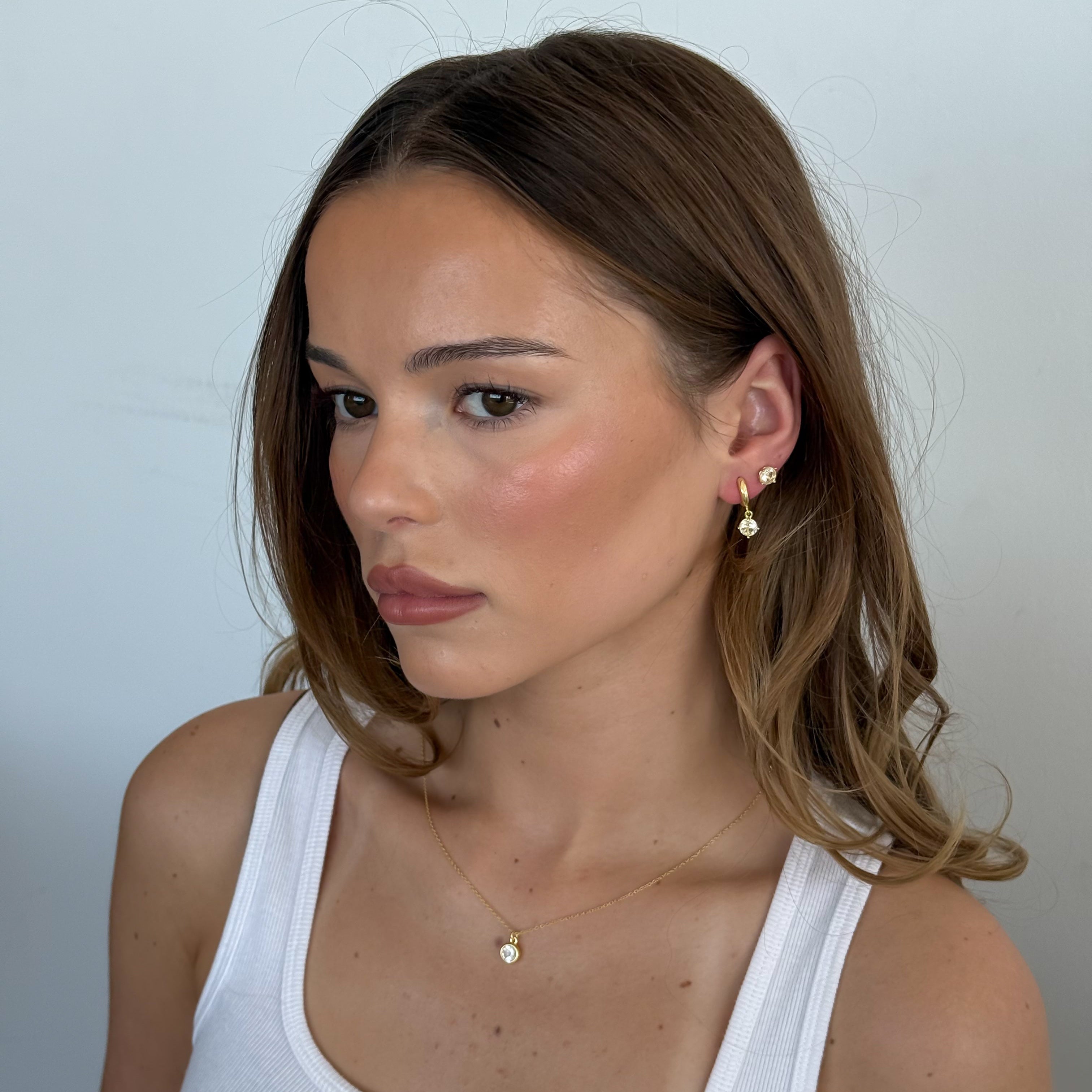 Woman wearing a white tank top with minimal jewelry against a plain background
