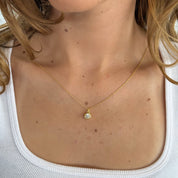 Close-up of a gold necklace with a pendant on a person wearing a white top.