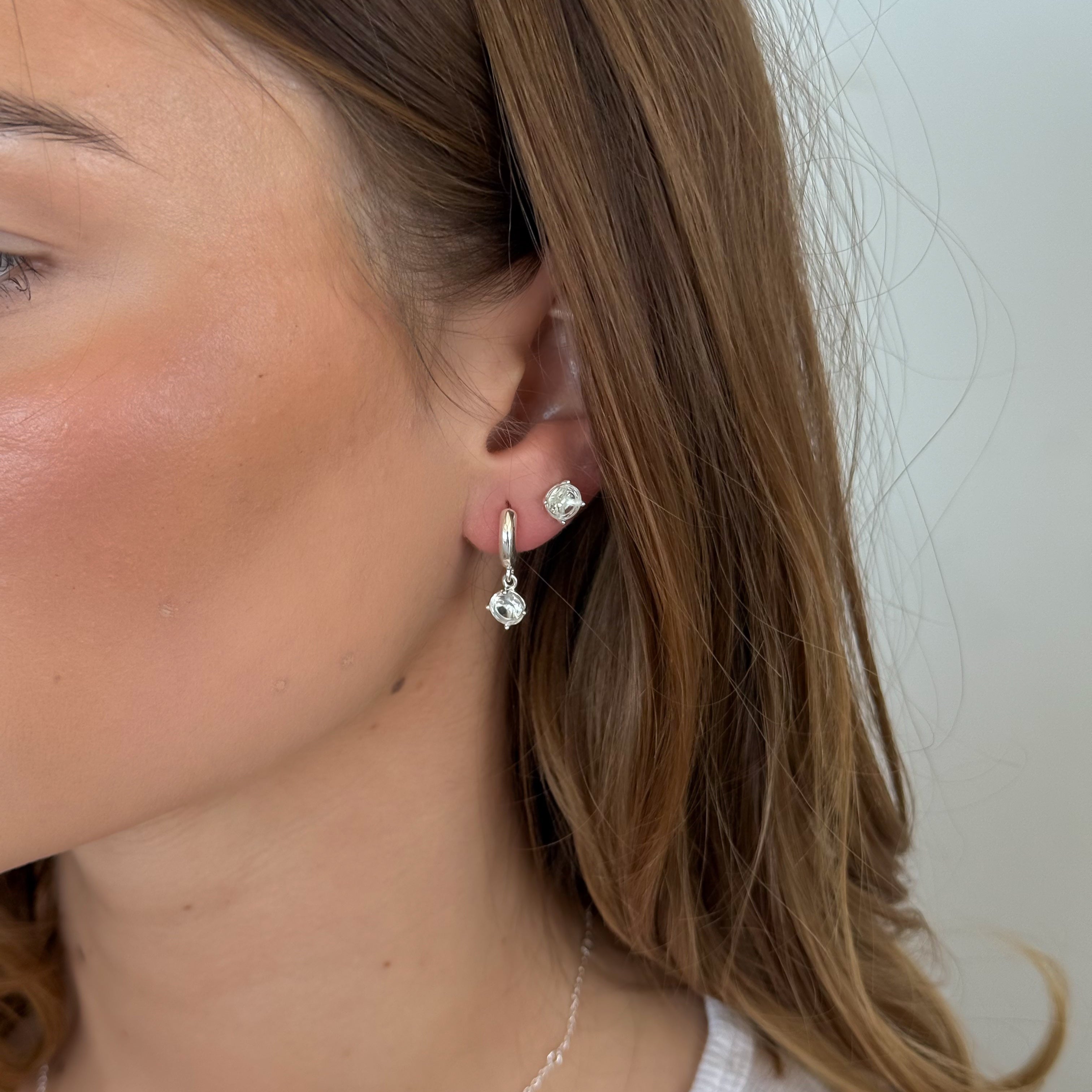 Close-up of a person wearing silver hoop earrings with a plain background