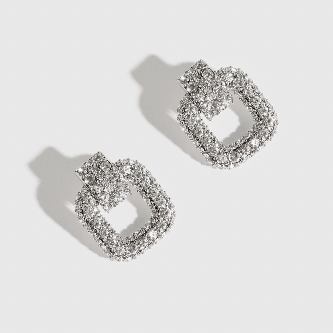 Silver plated buckle pavé stud earrings with cubic zirconia, shown on a plain background.
