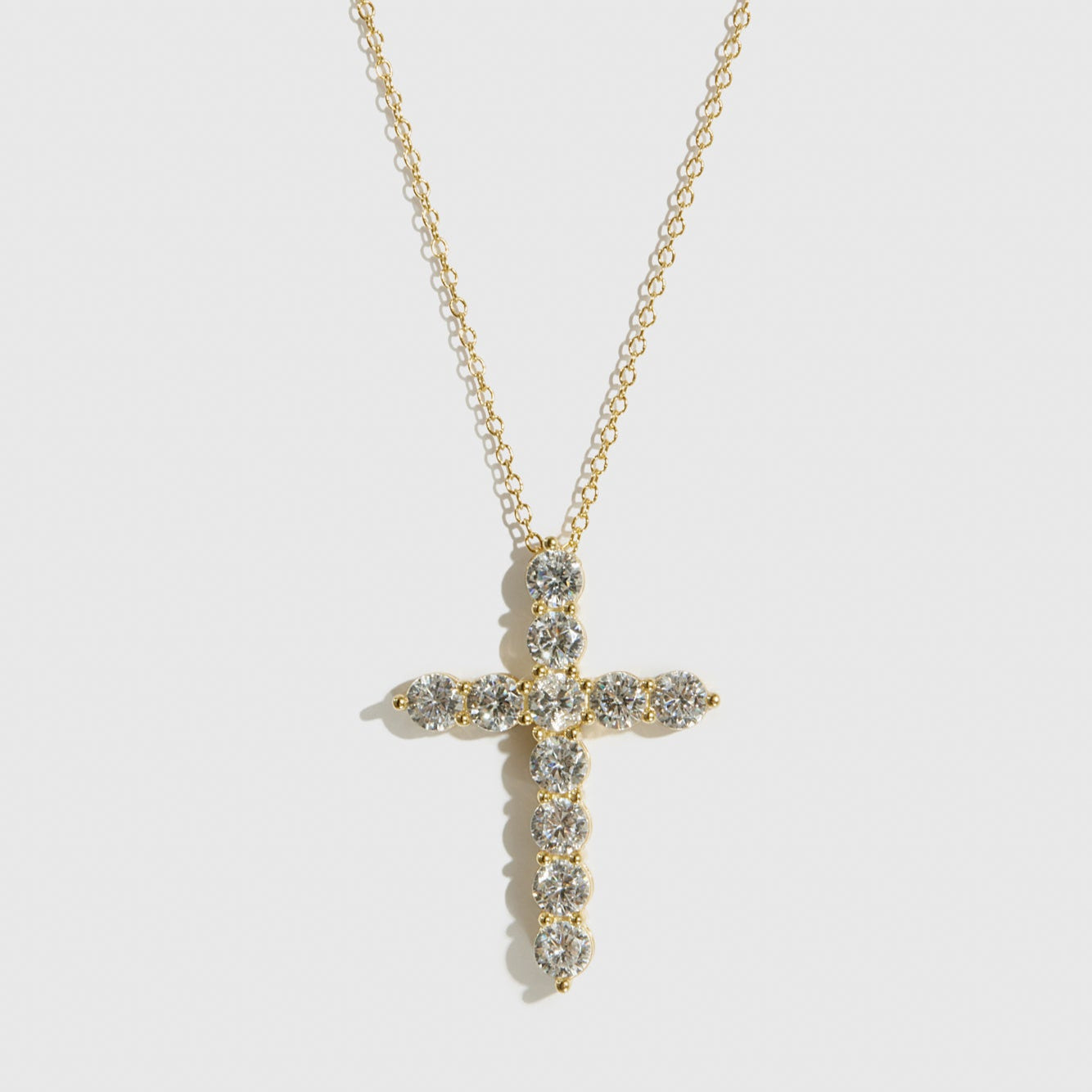 Gold cross necklace with clear stones on a white background