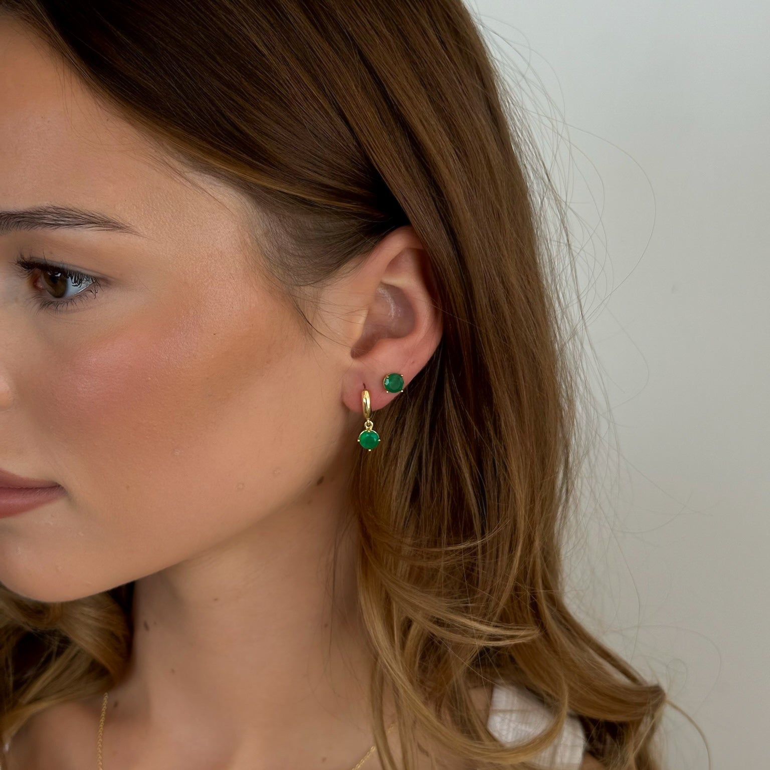 Close-up of a woman wearing green earrings with a neutral background