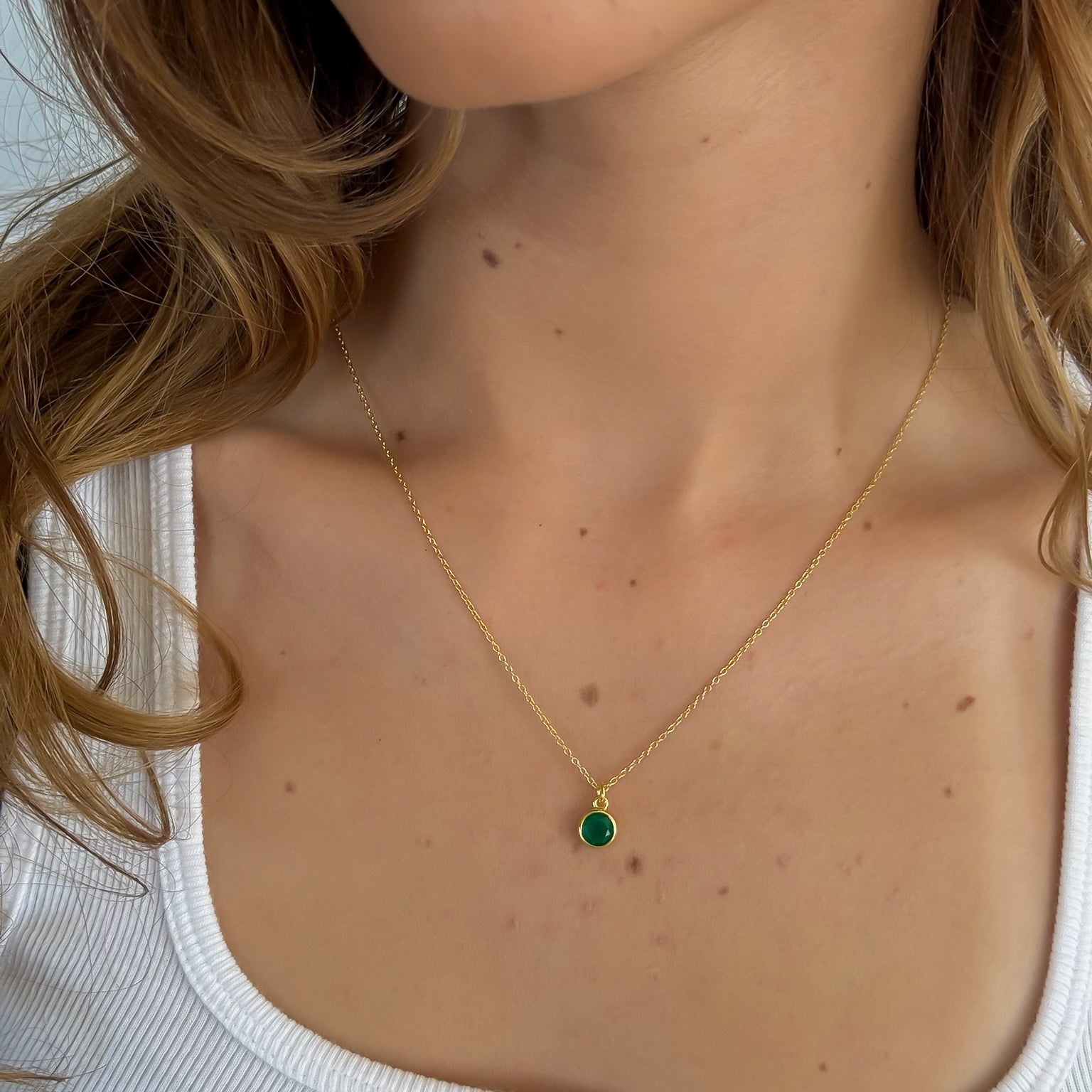 Close-up of a person wearing a gold necklace with a green gemstone pendant.