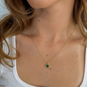 Close-up of a person wearing a gold necklace with a green gemstone pendant.
