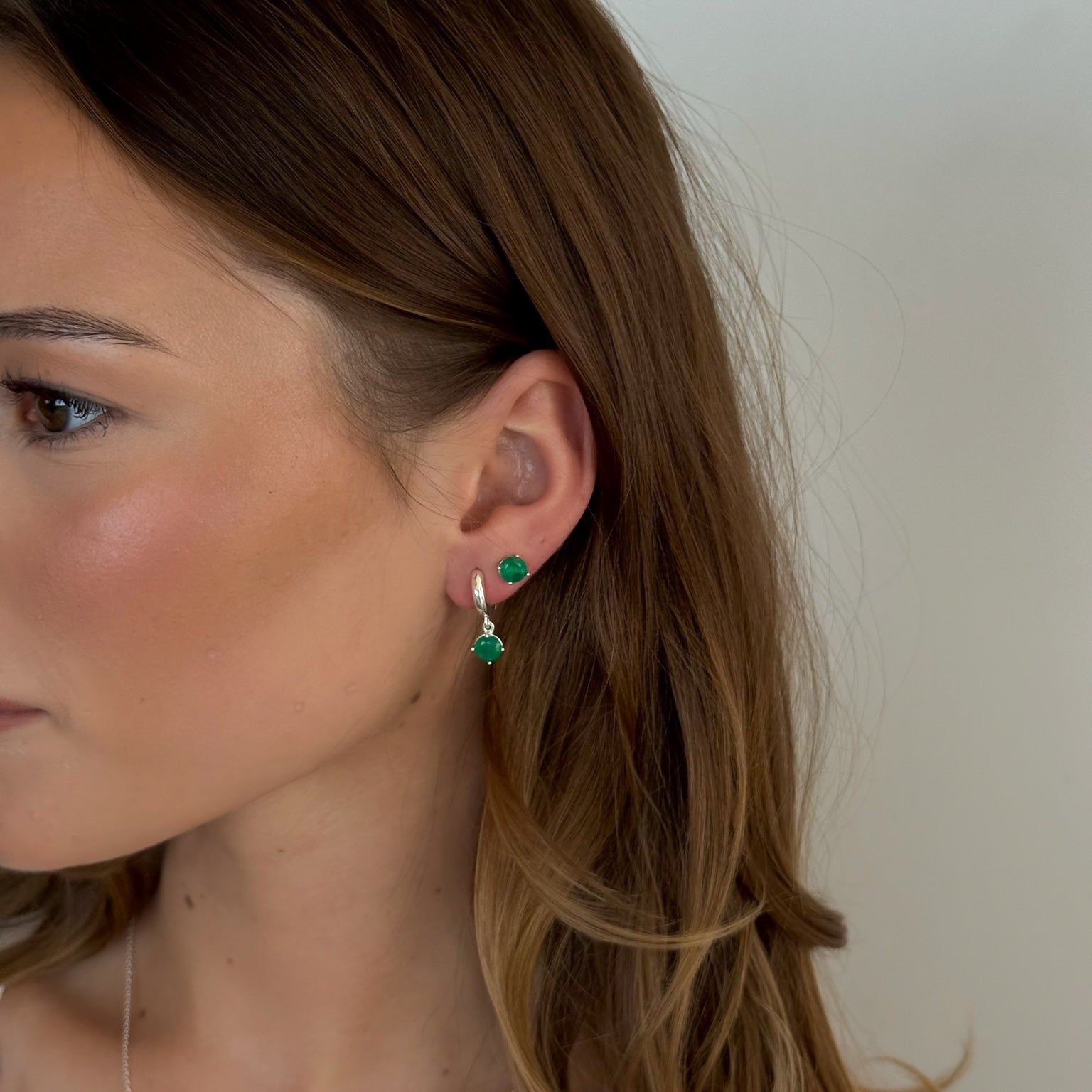 Close-up of a person wearing green earrings with a neutral background