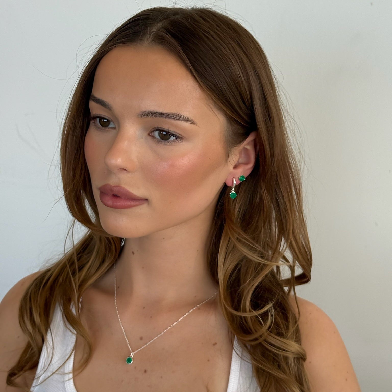 Woman wearing green earrings and a necklace against a plain background