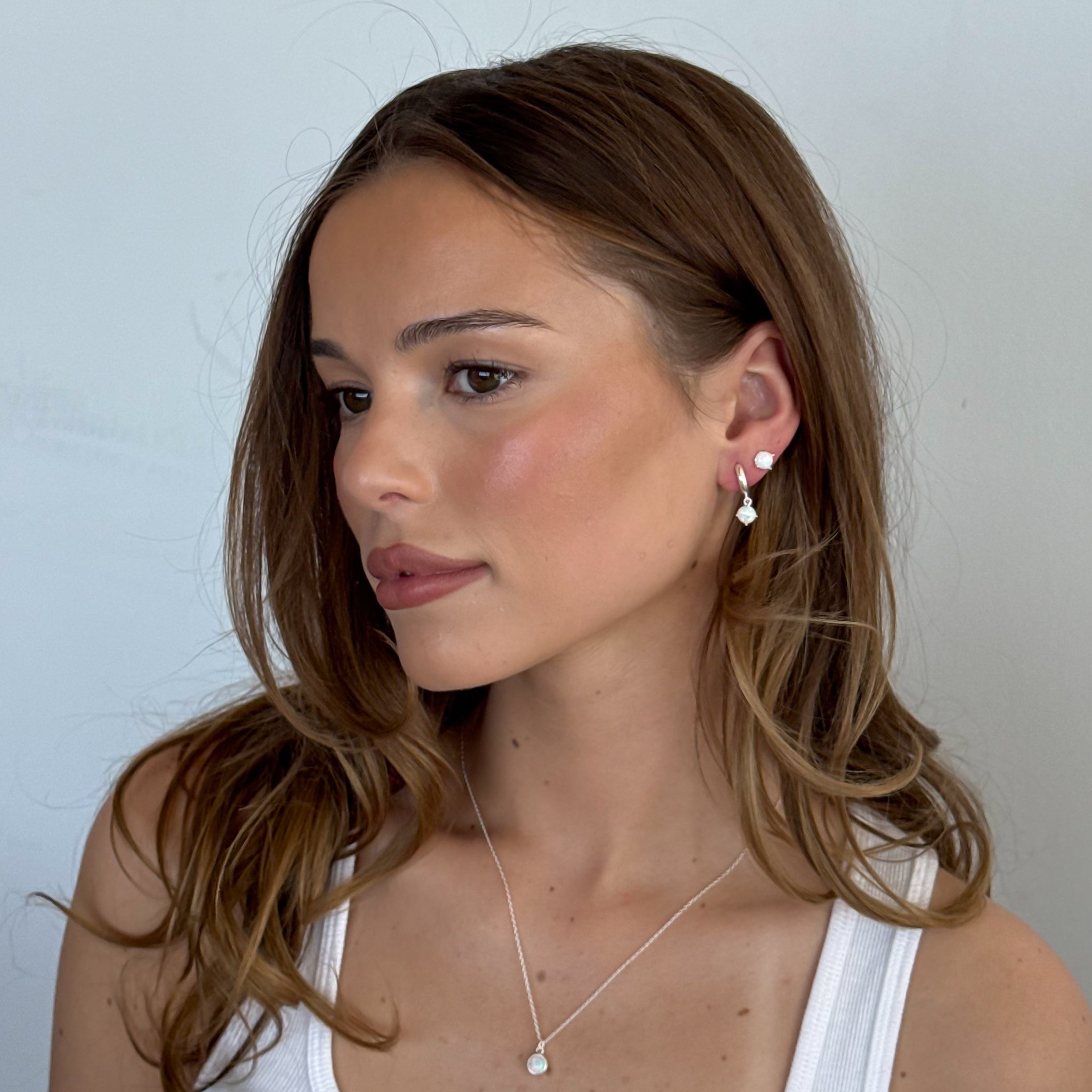 Woman wearing a white tank top and pearl earrings against a light background